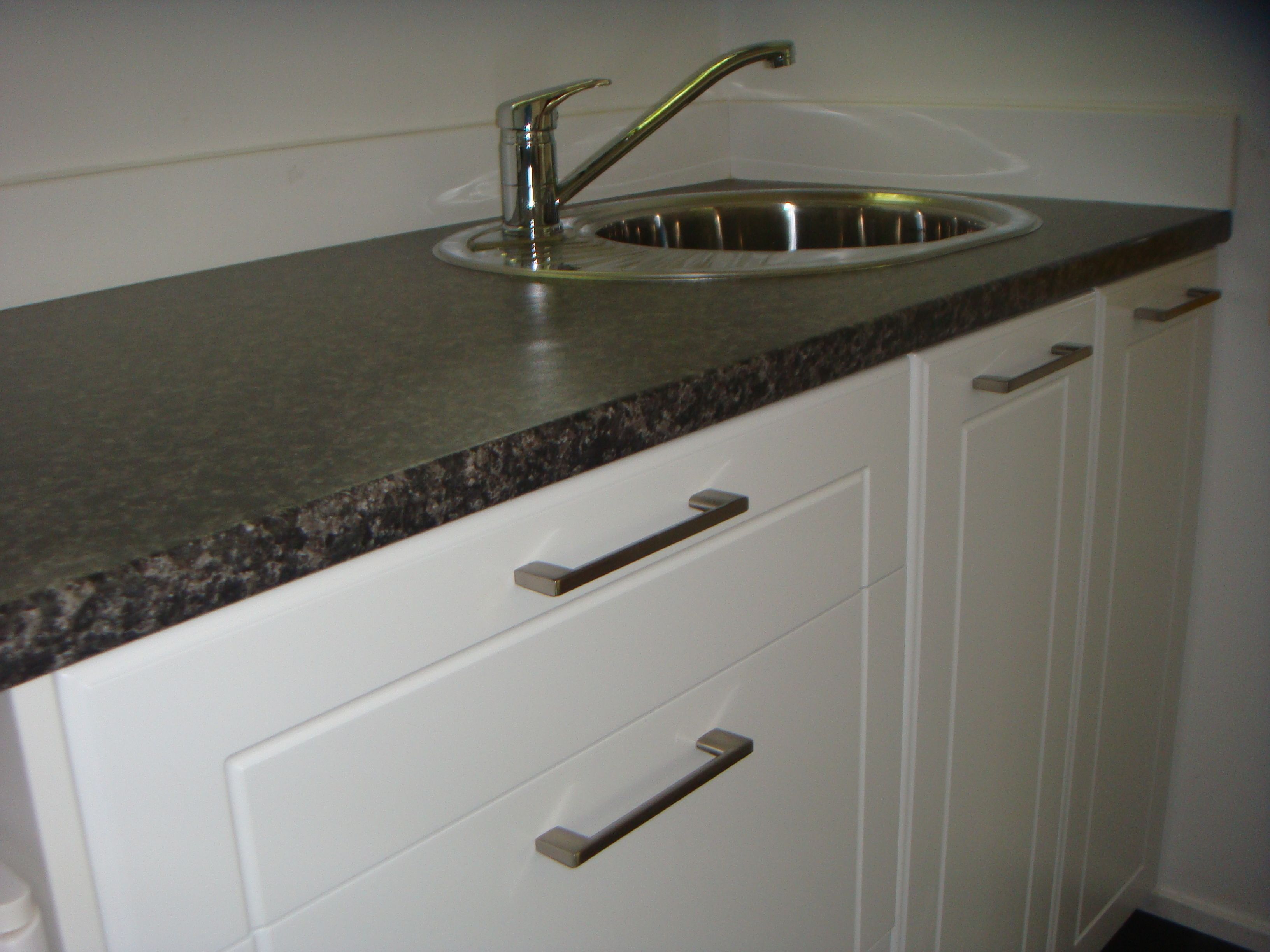 Una cocina con pileta de acero inoxidable, encimera de granito y muebles de cocina blancos.