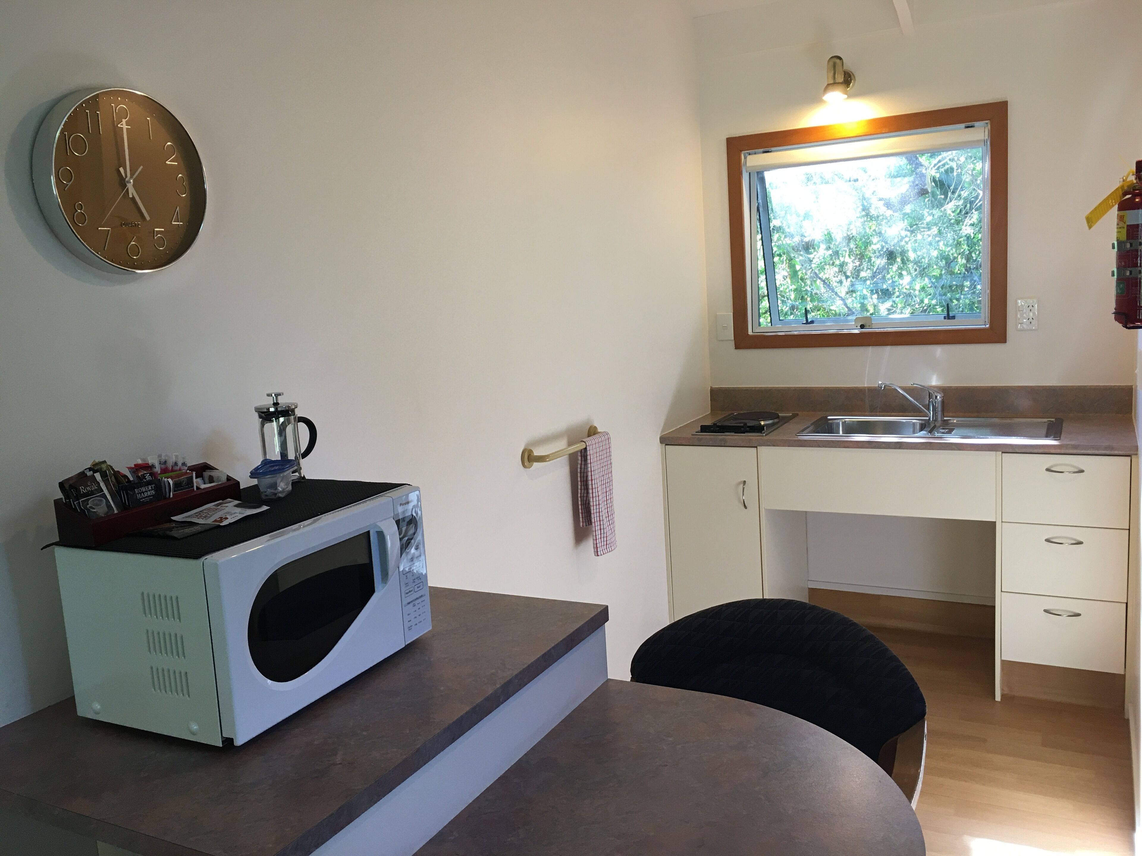 A compact kitchen with a microwave, a sink, and a window with a view of greenery.