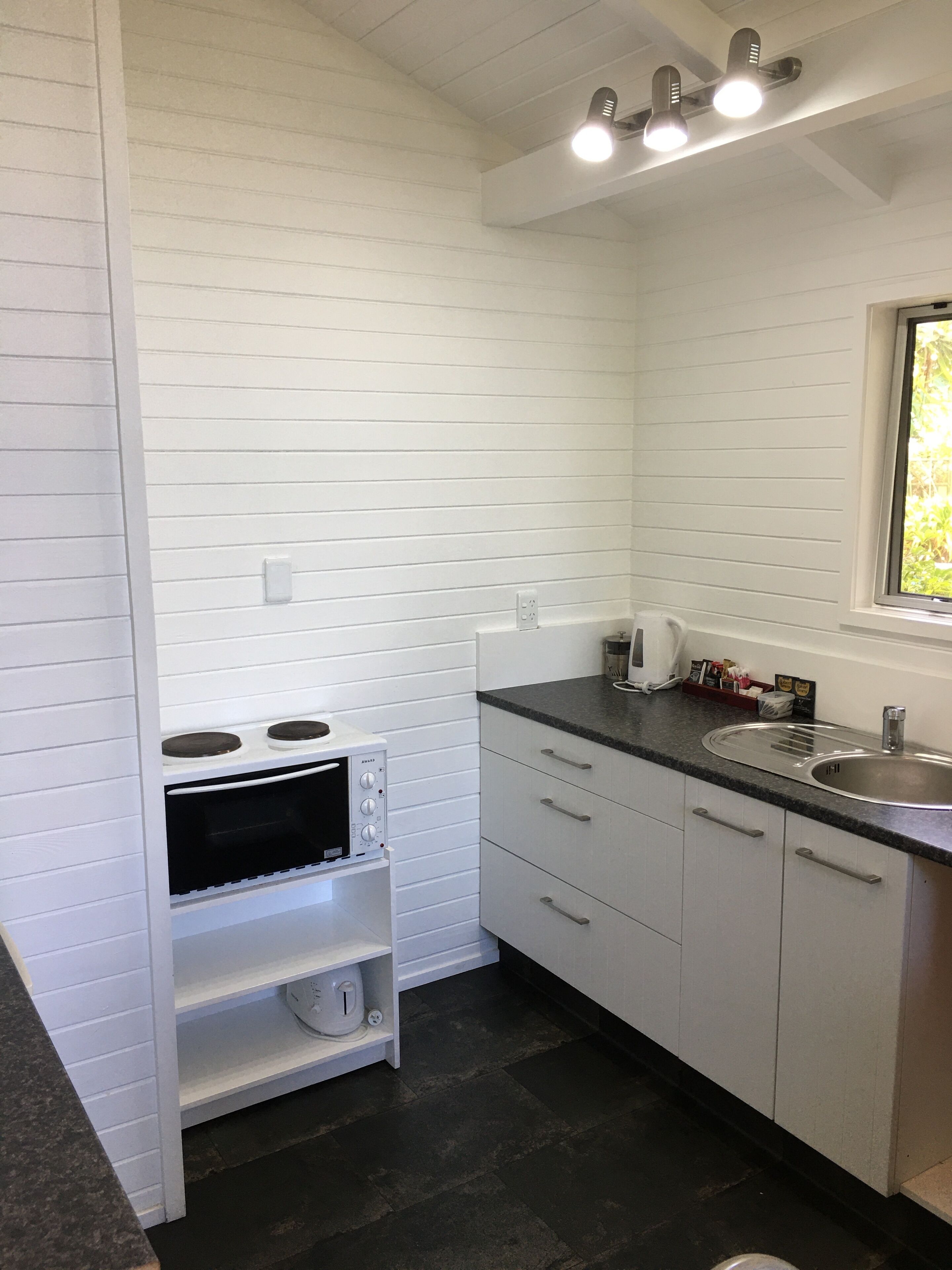A compact kitchen with white cabinetry, a built-in oven, a sink, and a window providing natural light.