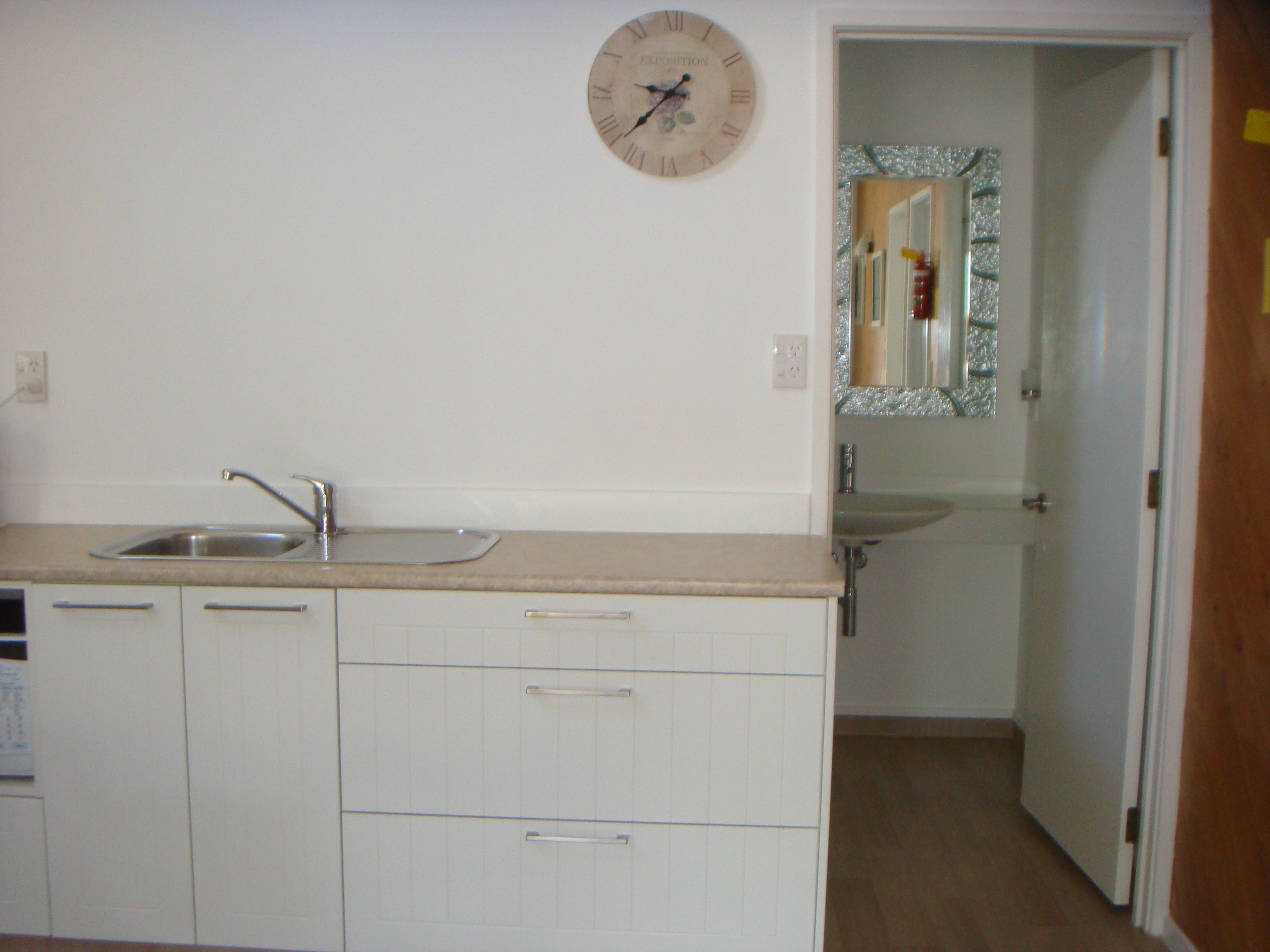 Una cocina con un lavamanos, armarios y un reloj de pared.