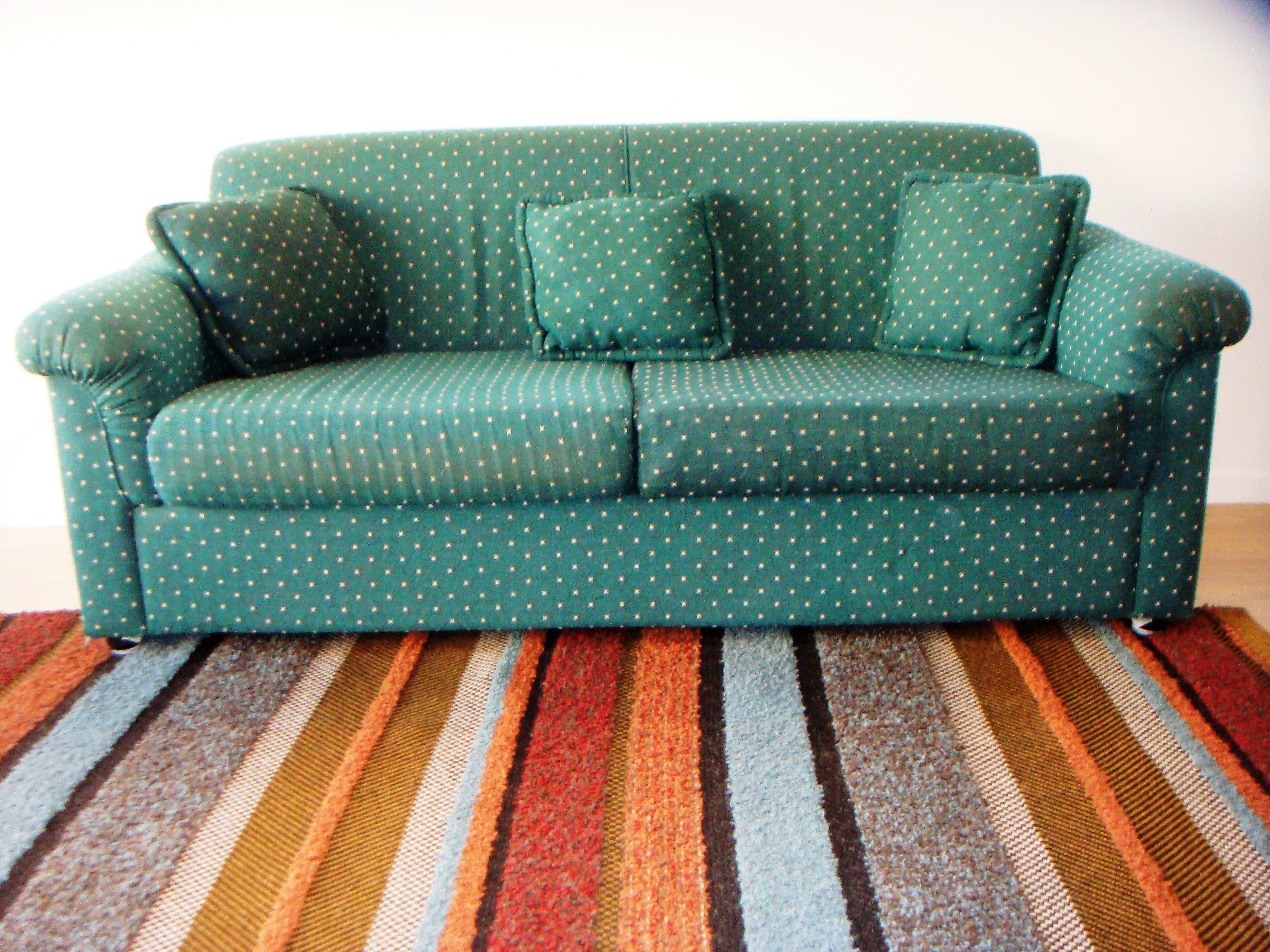 Un canapé vert à motifs à pois, agrémenté de plusieurs coussins, est posé sur un tapis rayé.