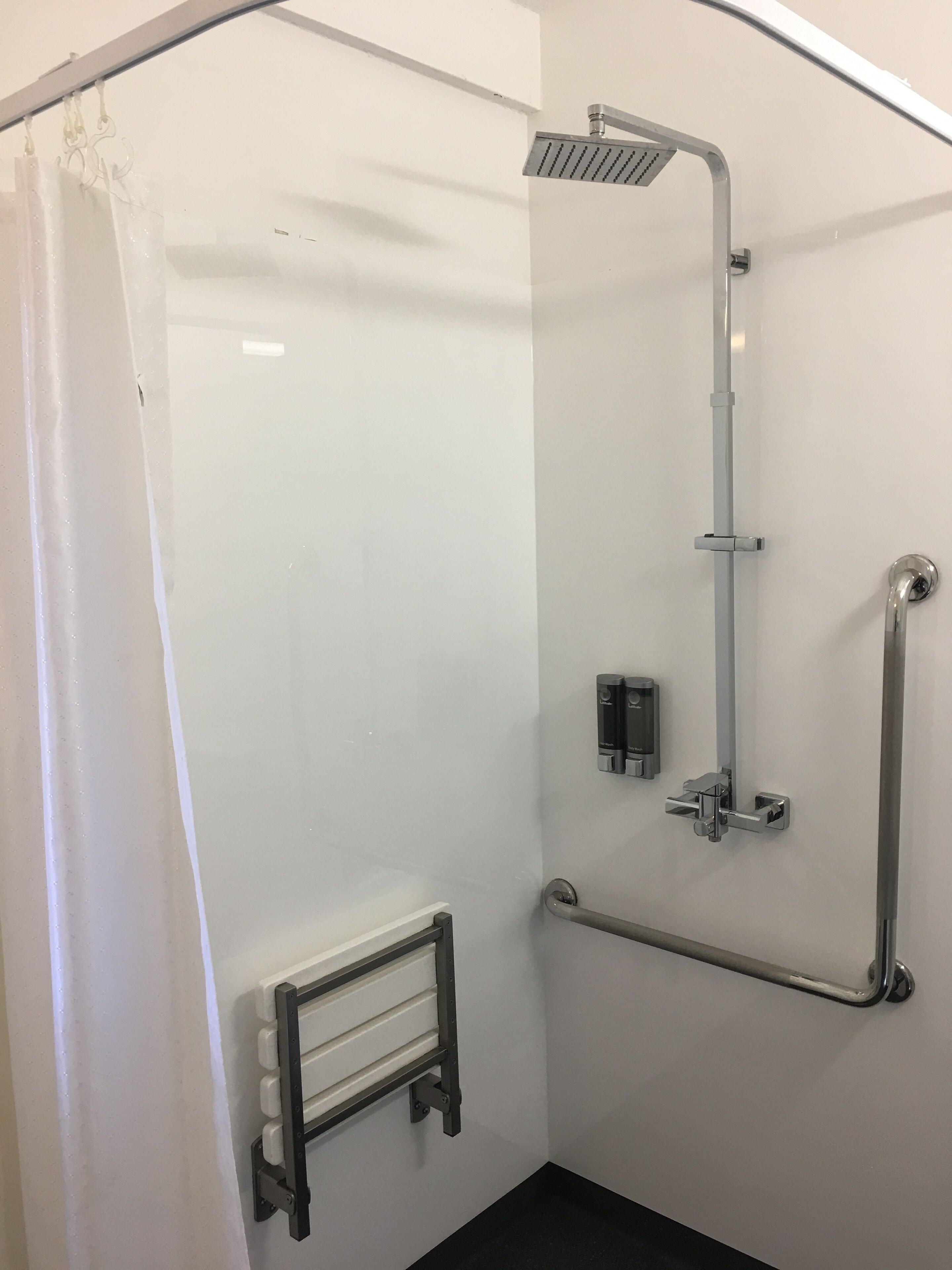 A modern shower with a handheld showerhead, a handheld shower control, and a grab bar.