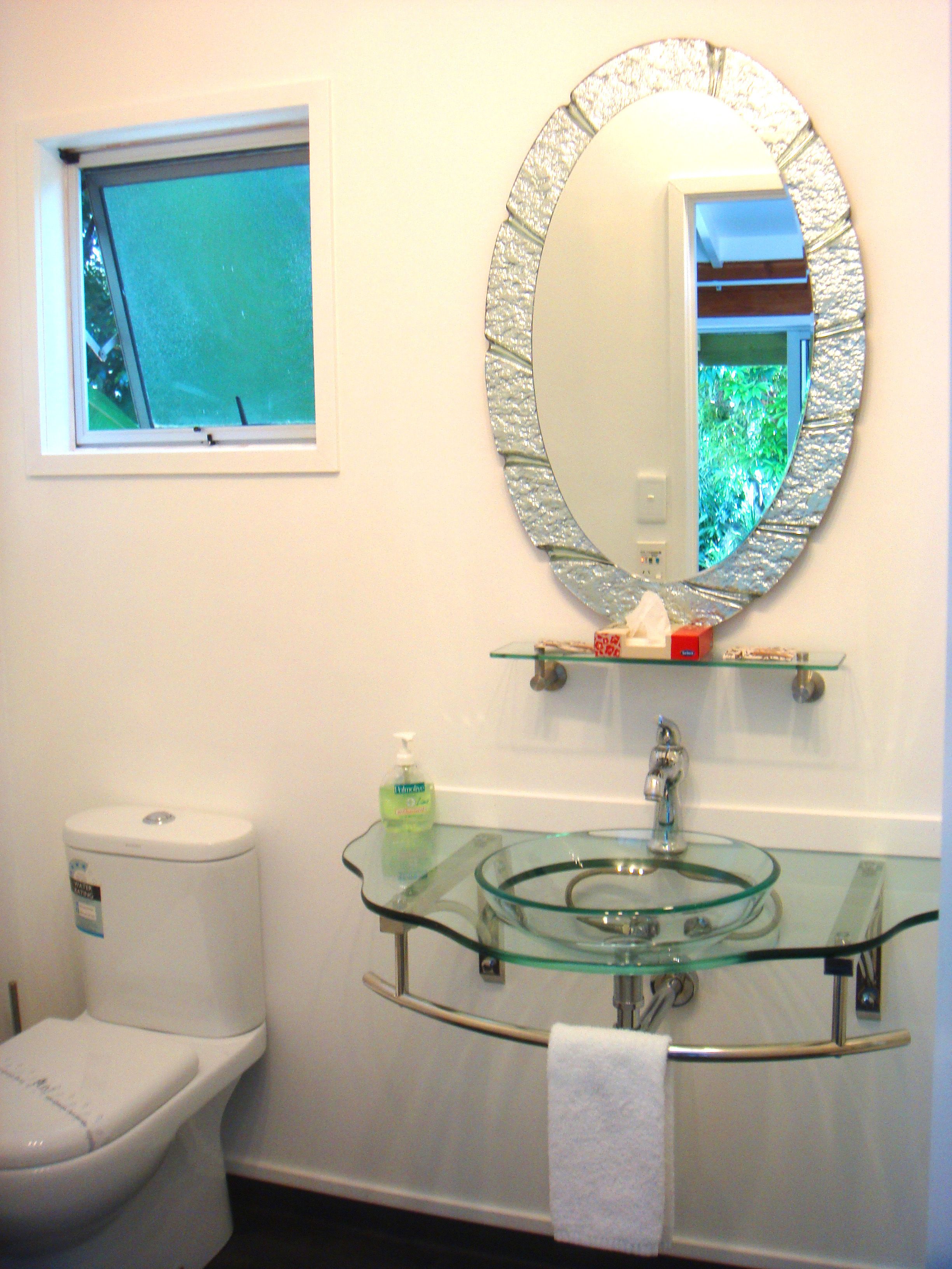 A bathroom with a glass sink, a toilet, a mirror, and a window.