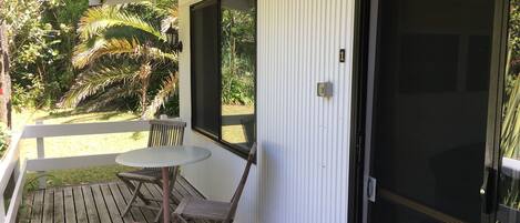 A wooden deck with a table and chairs, a door, and a view of a garden with palm trees.