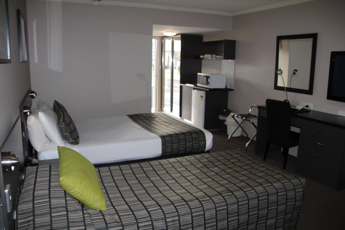 A hotel room with a bed, a desk, a chair, a microwave, and a television.