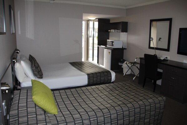 Una habitación de hotel con cama, escritorio, silla, microondas y televisión.