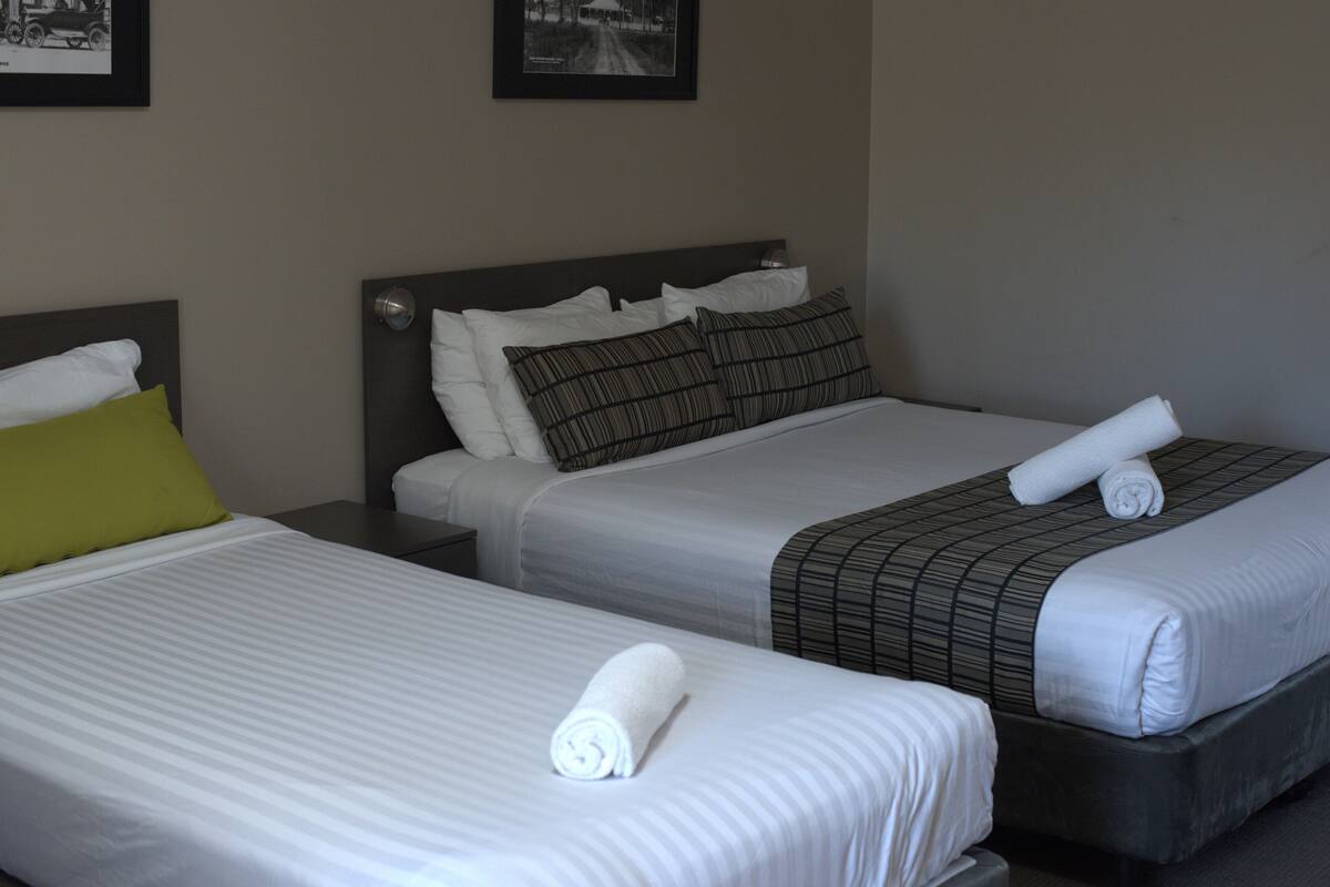Two adjacent hotel beds with white linens, pillows, and rolled towels.