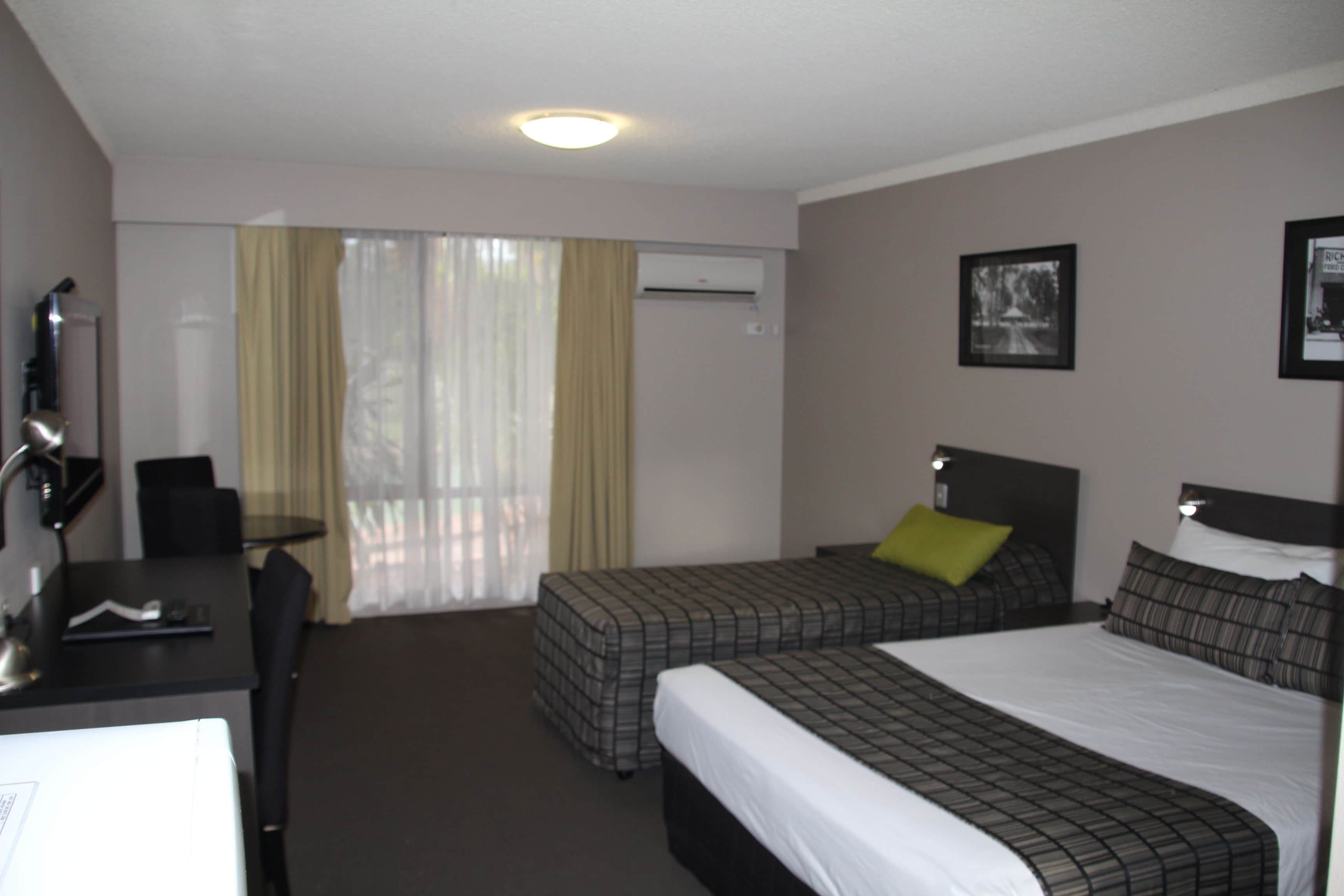 Ein Hotelzimmer mit zwei Betten, einem Schreibtisch, einem Stuhl und einer Klimaanlage.
