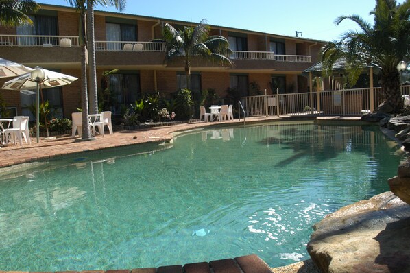Un hotel con piscina, mobiliario exterior y palmeras.