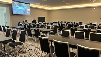 A conference room with multiple tables and chairs, a large screen for presentations, and a patterned carpet.