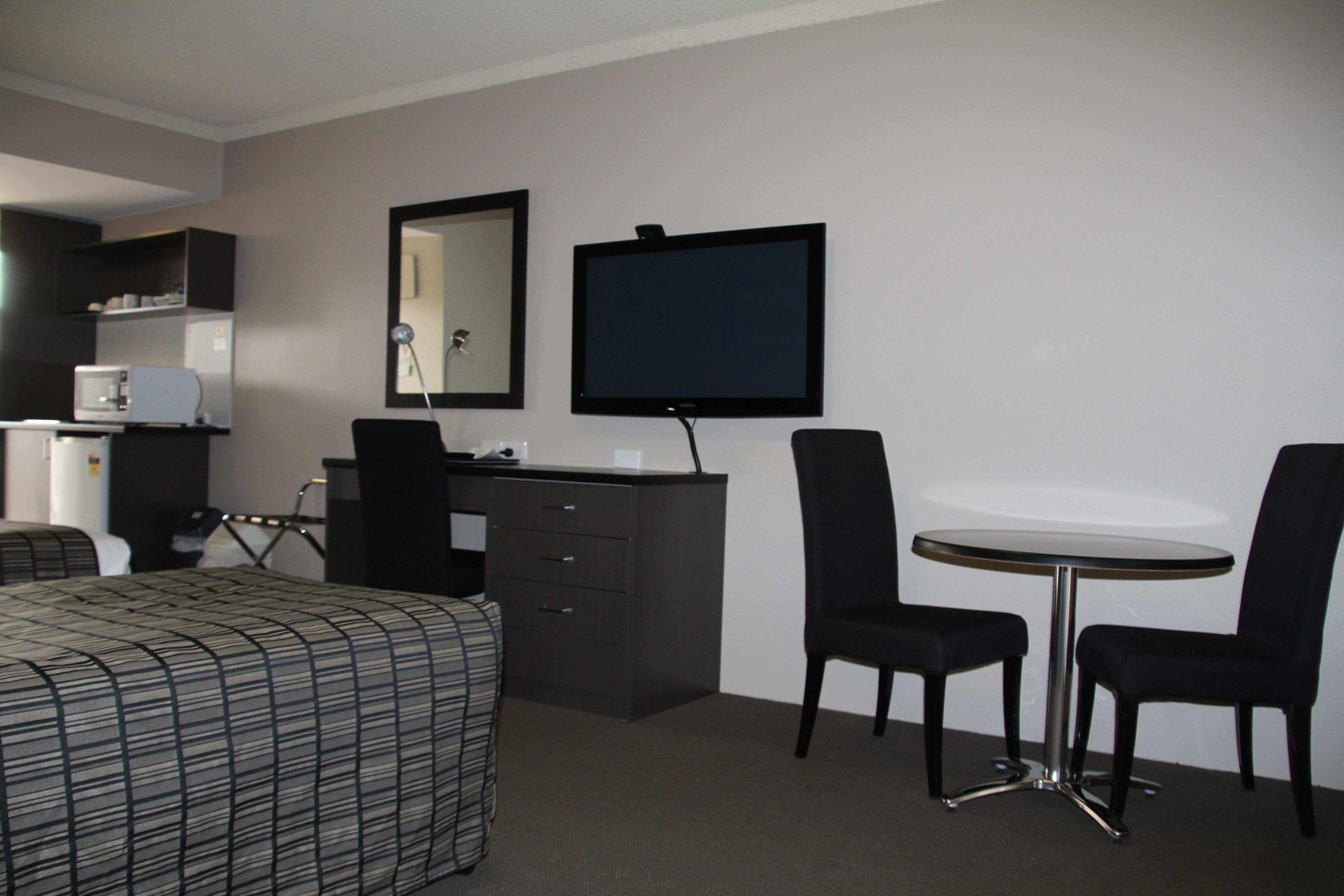 Habitación de hotel con cama, escritorio, silla, mesita, espejo y televisor.