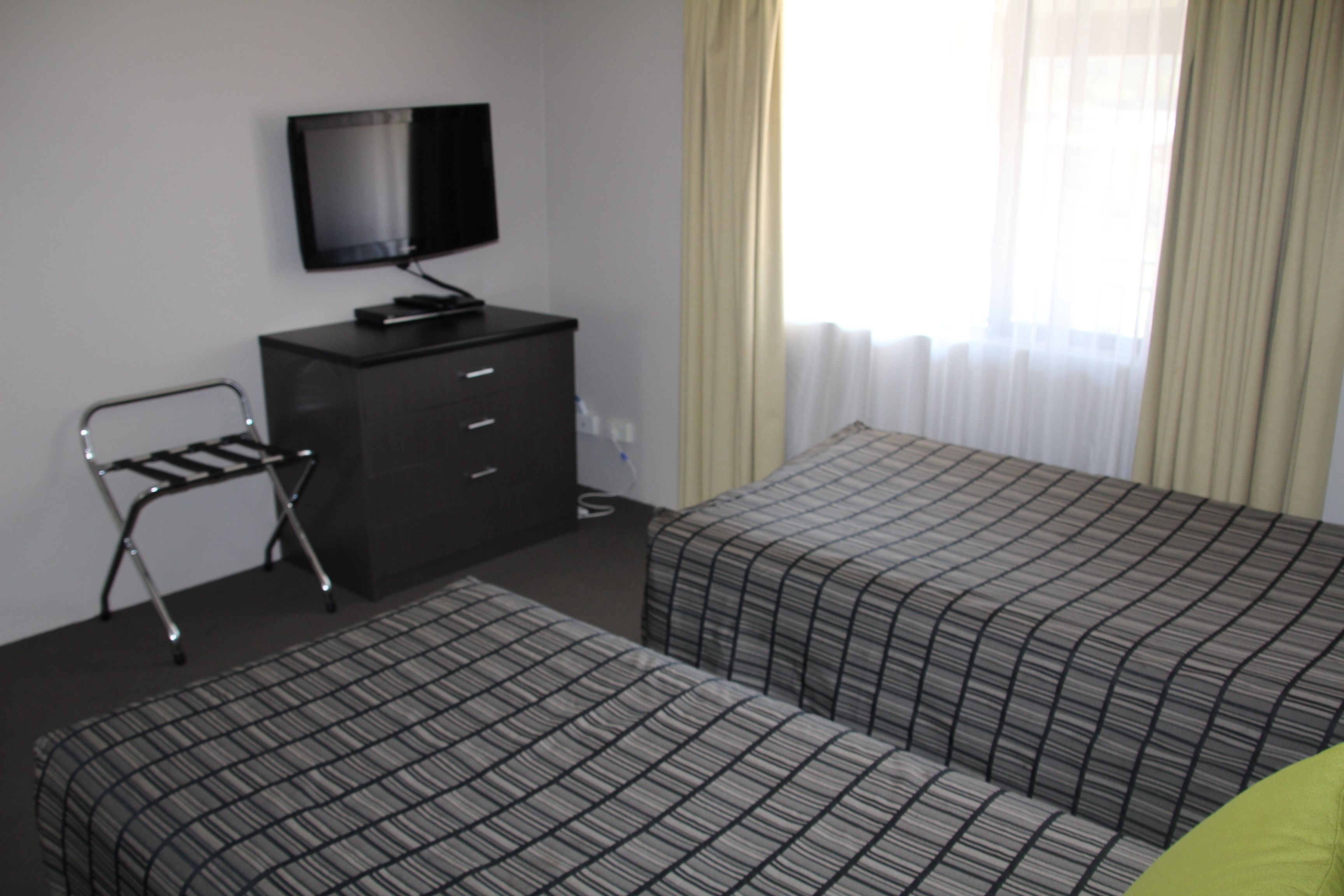 Habitación de hotel con dos camas, un televisor en una cómoda y una ventana con cortinas.