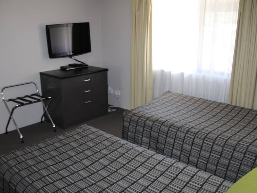 Habitación de hotel con dos camas, un televisor en una cómoda y una ventana con cortinas.