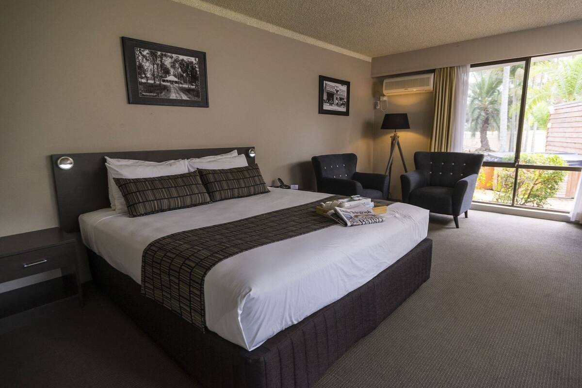 A hotel room with a large bed, two armchairs, a desk, and a window with a view of palm trees.