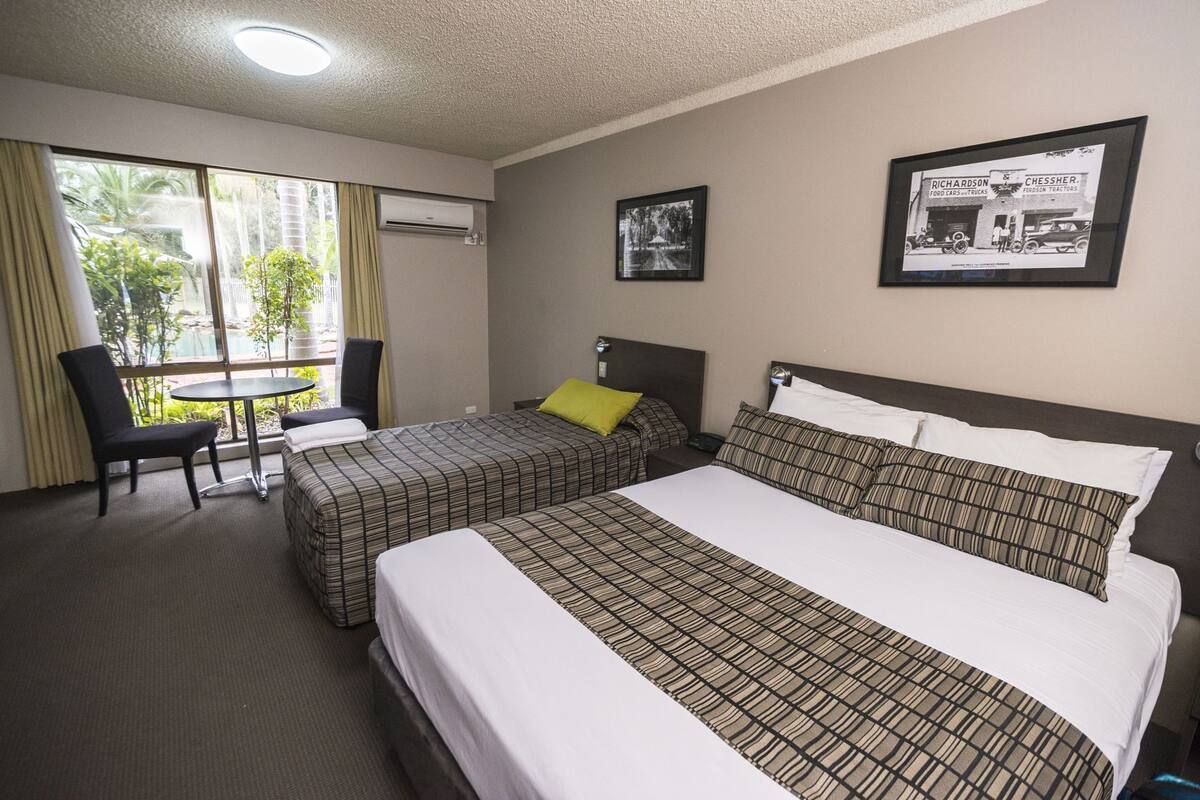 A hotel room with two beds, a dining table, a chair, and a window with curtains.