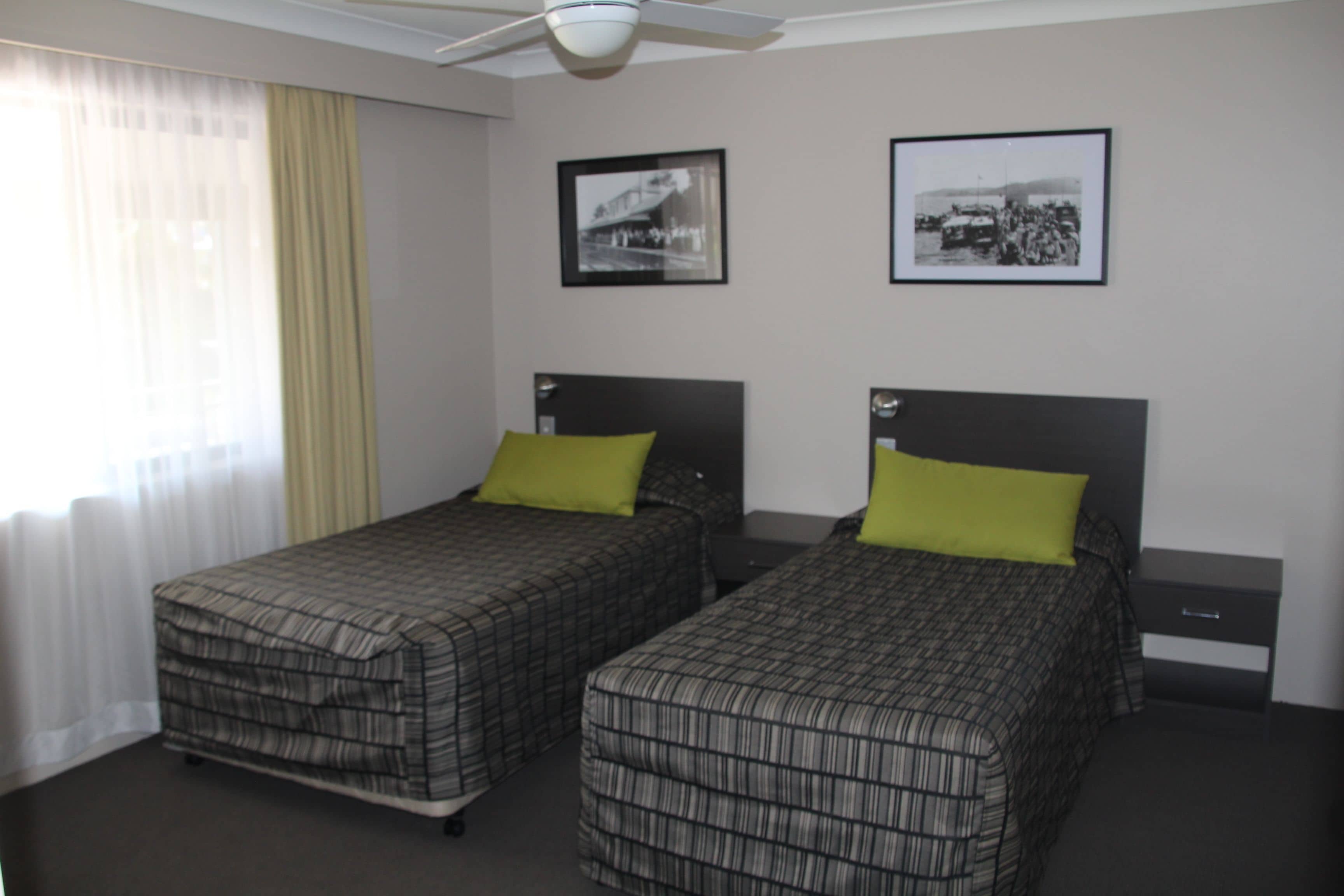 A hotel room with two single beds, a ceiling fan, and two framed pictures on the wall.
