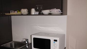 Une cuisine compacte équipée d’un four à micro-ondes, d’un petit réfrigérateur, d’un évier et de deux poubelles.