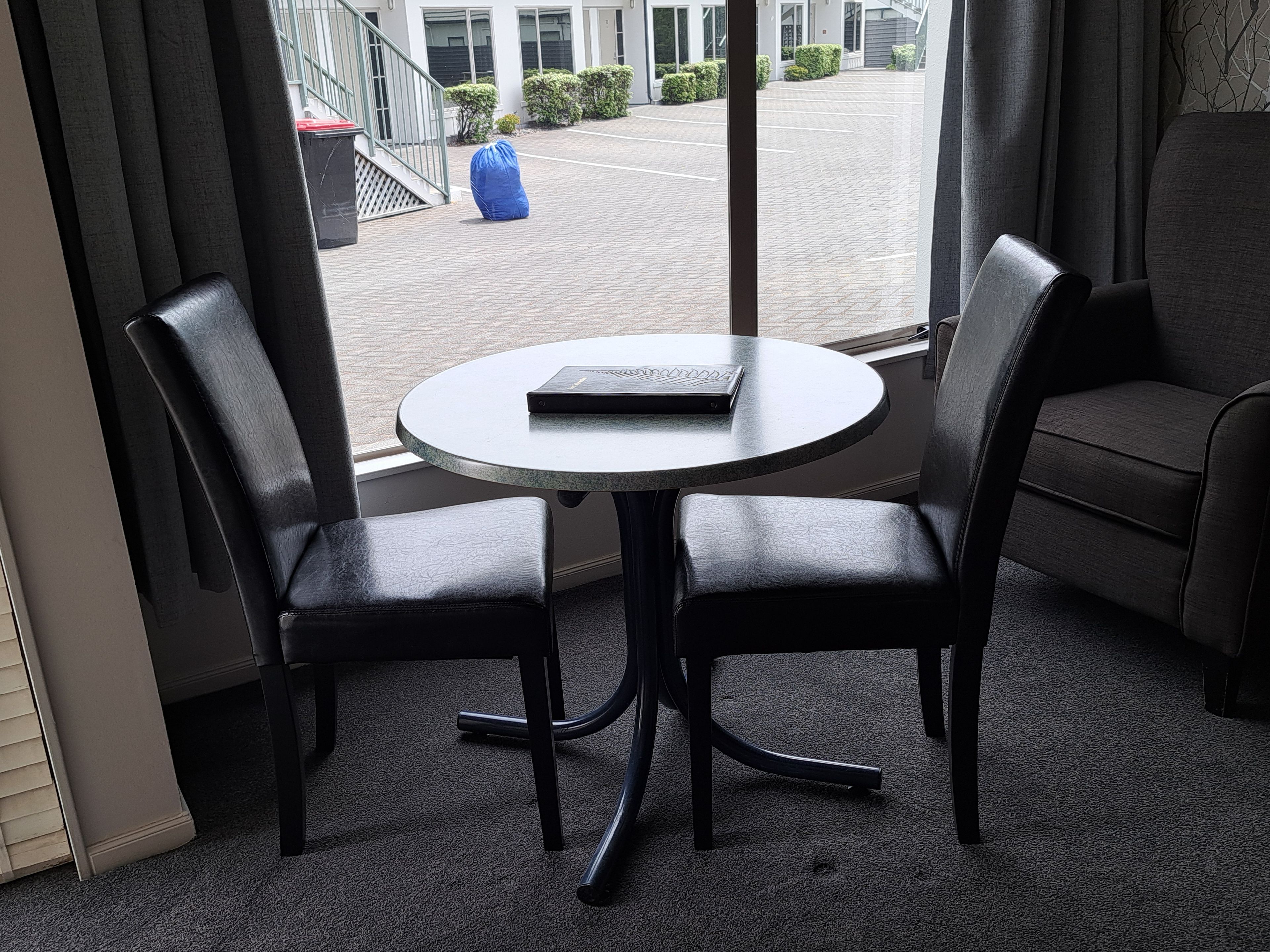 Une pièce avec une table ronde et deux chaises, un canapé et une vue sur un bâtiment à l’extérieur.