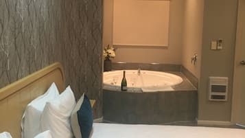 A hotel room with a bed, a large window, a wall-mounted air conditioner, and a bathroom with a bathtub and a towel rack.