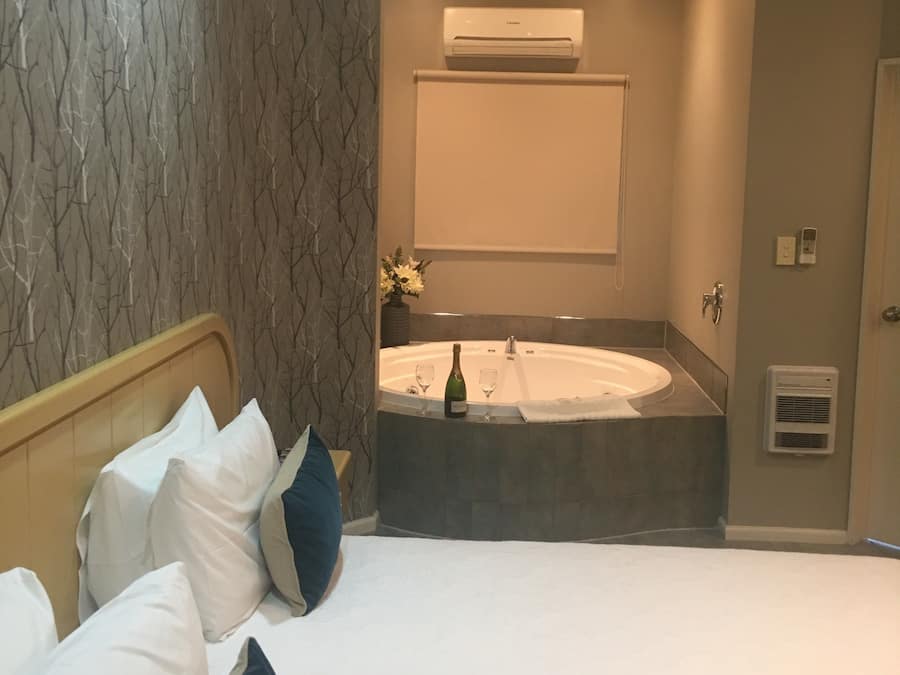Habitación de hotel con cama, un ventanal grande, aire acondicionado de pared y baño con bañera y perchero para toallas.
