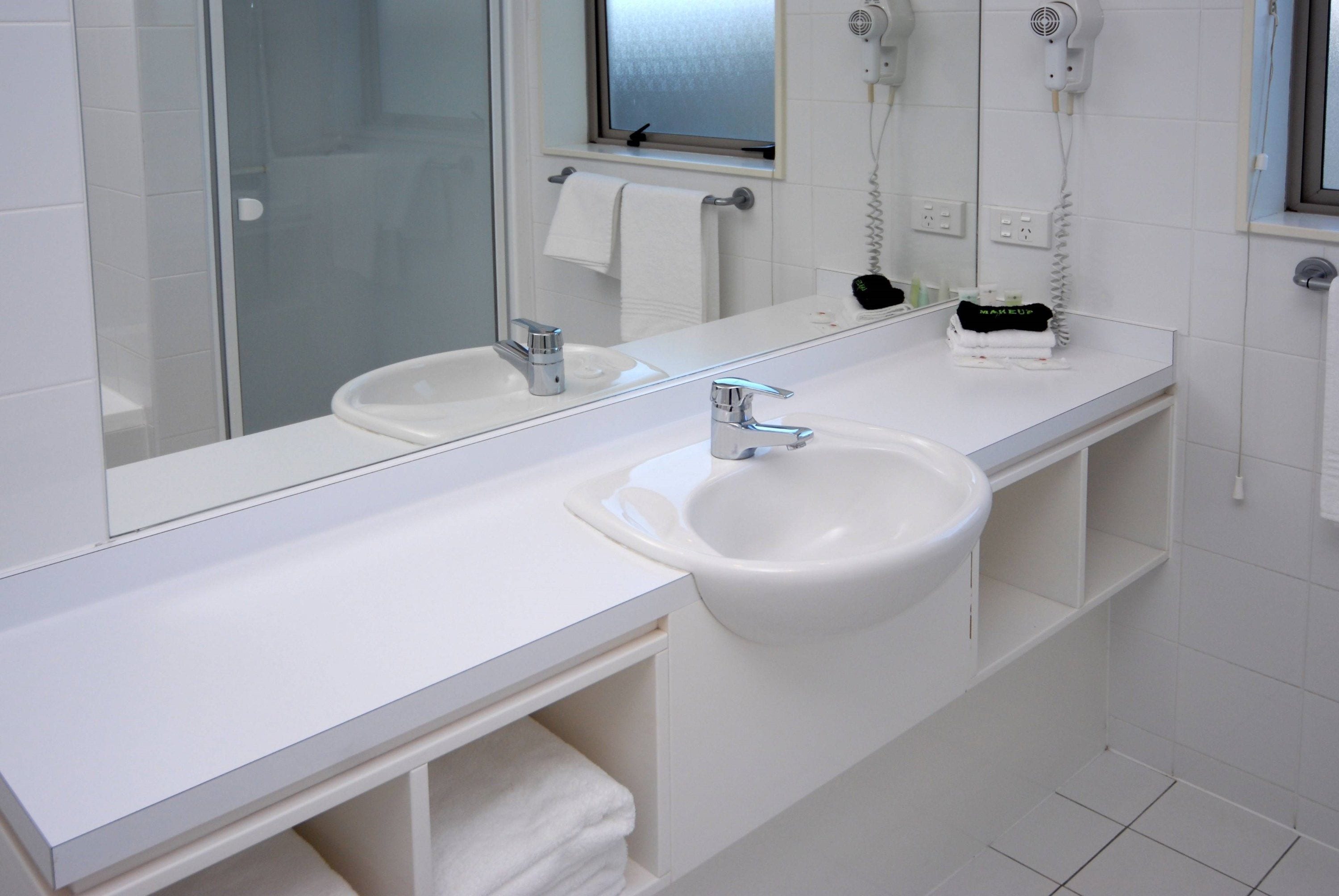 A modern bathroom with two sinks, a large mirror, and a hairdryer on the wall.