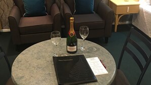 A room with two armchairs, a table with a bottle of champagne, two glasses, a menu, and a nightstand with a lamp.