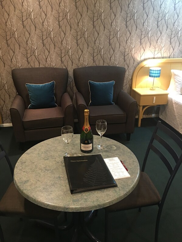 Una habitación con dos sillones, una mesa con una botella de champán, dos copas, un menú y una mesita de noche con una lámpara.