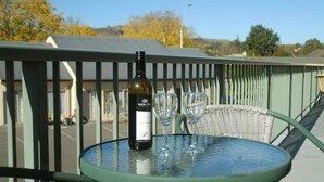 A table with a bottle of wine and two wine glasses on a balcony railing.