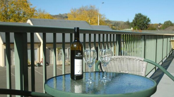 A table with a bottle of wine and two wine glasses on a balcony railing. - Village Motel (Havelock North)