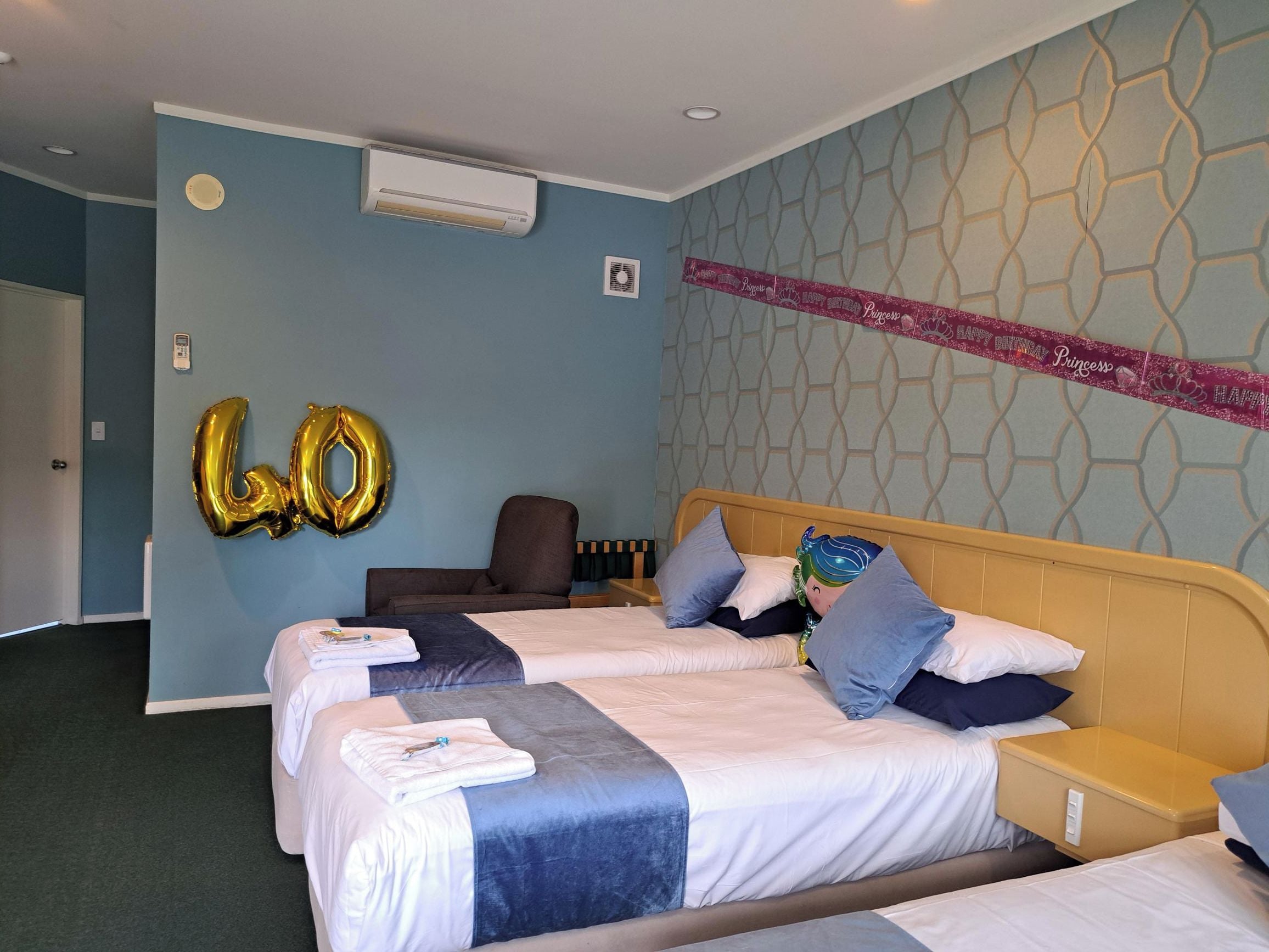 A hotel room with two beds, a wall-mounted air conditioner, and a decorative banner.