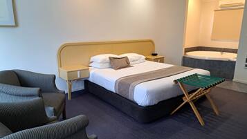 Una habitación de hotel con cama, mesitas de noche, una silla, un banco, una bañera y un espejo.