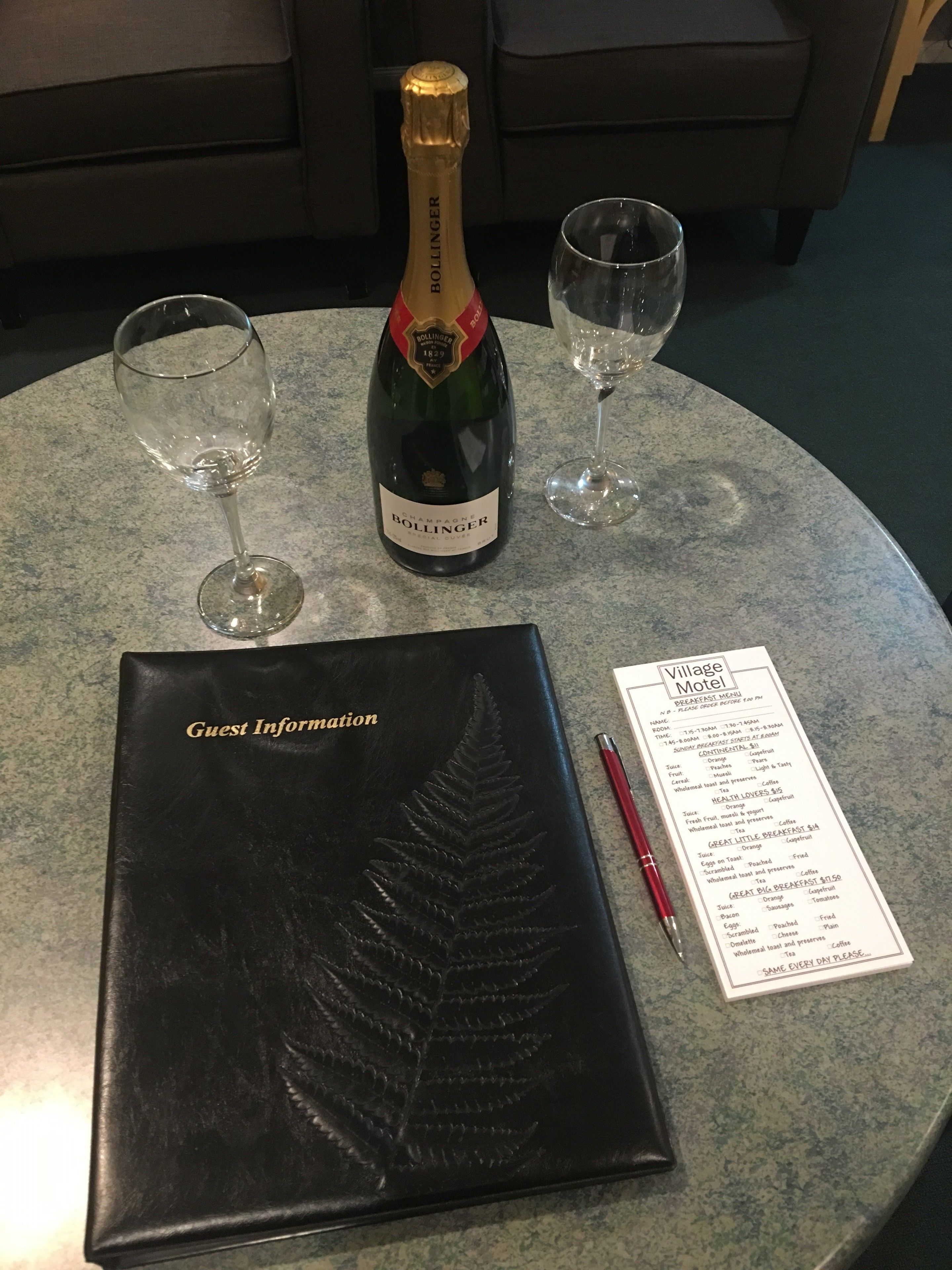 Una botella de Bollinger champagne, dos copas de vino vacías, un folleto informativo para huéspedes negro y un menú sobre una mesa redonda.