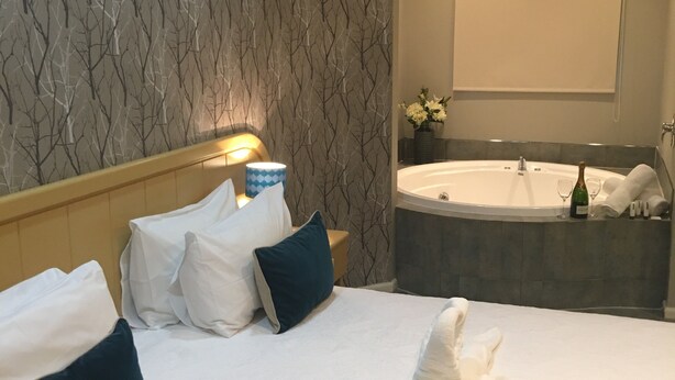 A hotel room with a large bed, a bathtub, and a wall-mounted air conditioning unit.