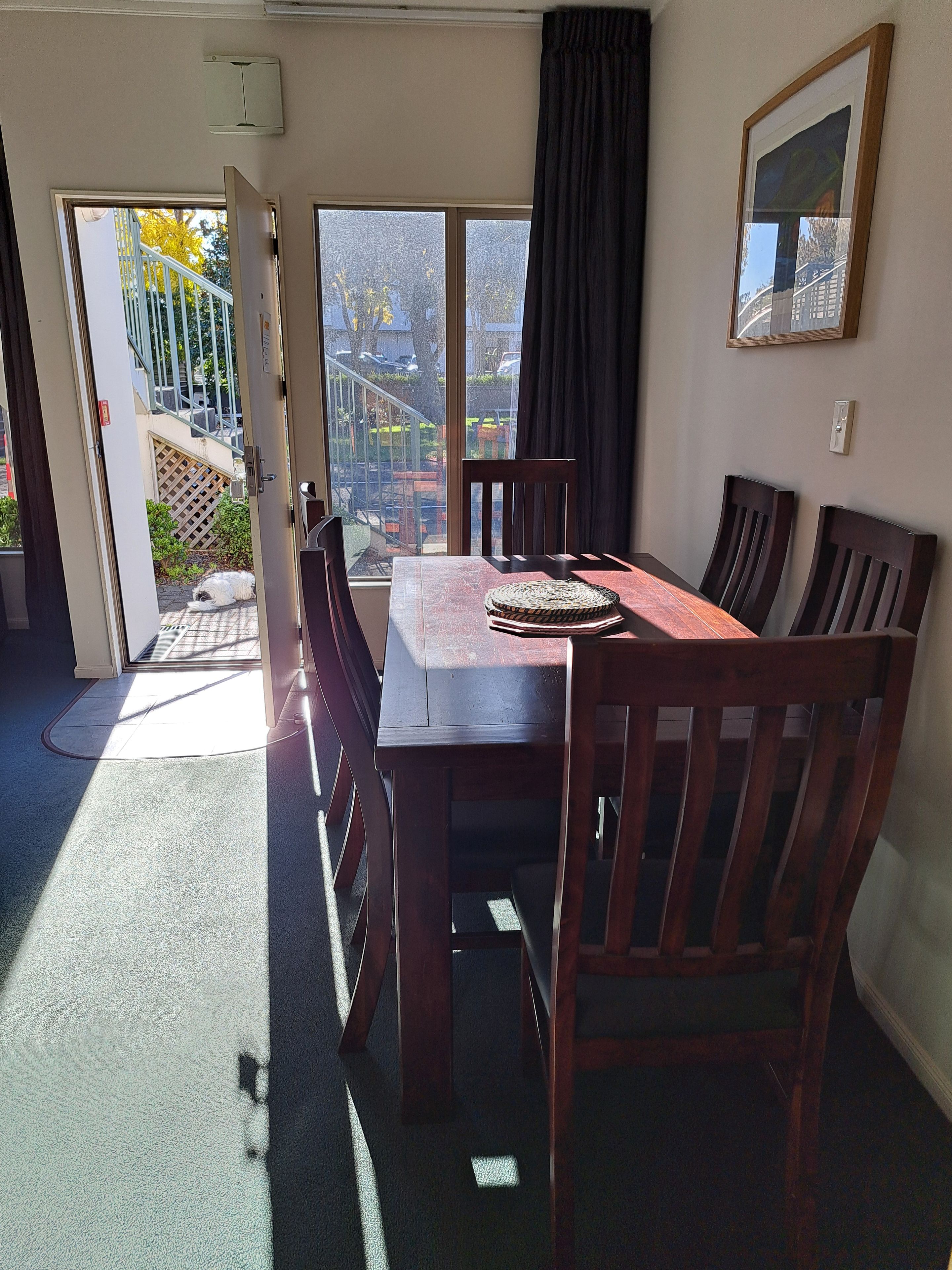 Un comedor con una mesa y sillas, un ventanal corredero que da al exterior, y un cuadro en la pared.
