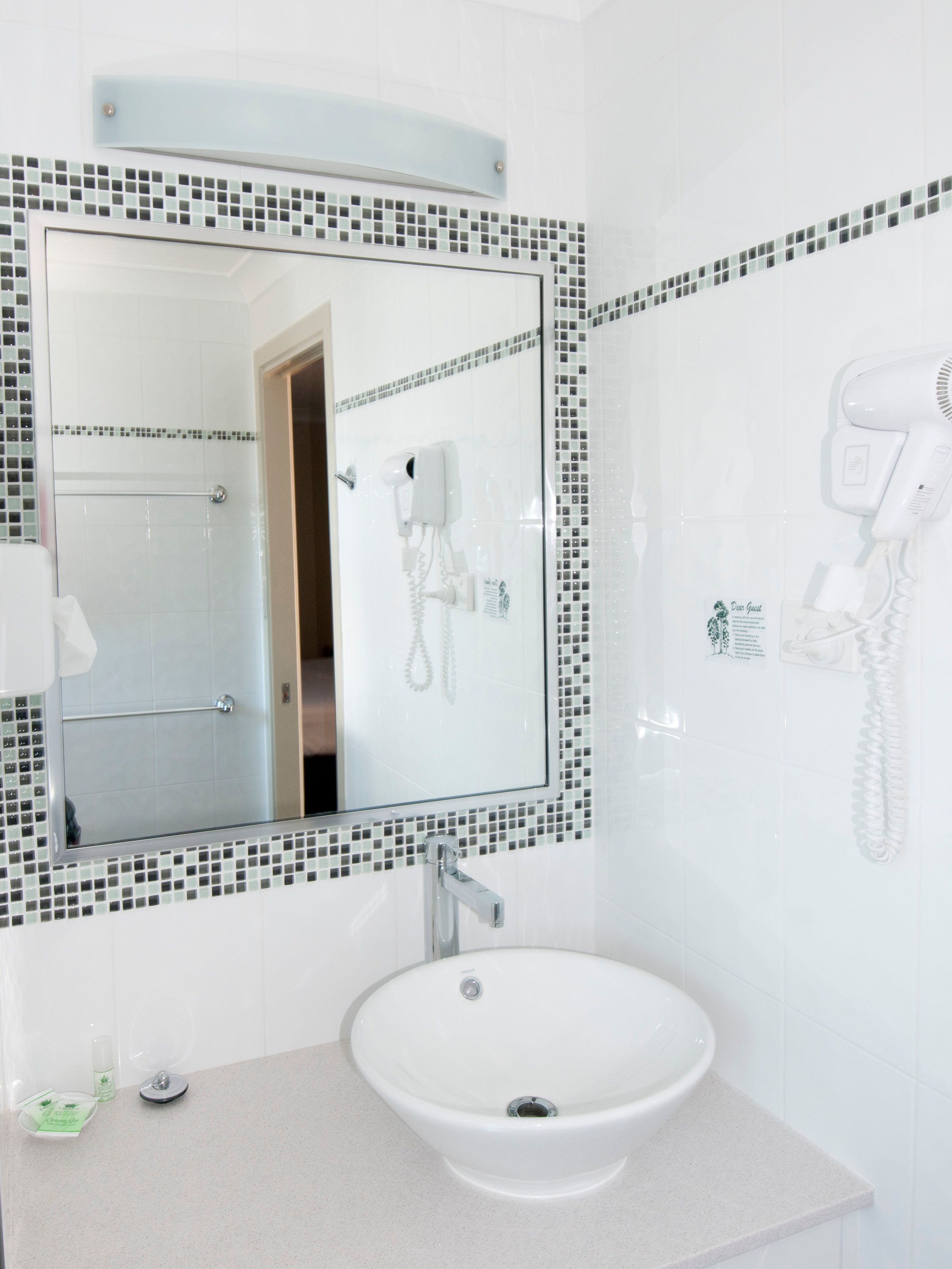 A bathroom with a white sink, a mirror with mosaic tiles, and a hairdryer mounted on the wall.