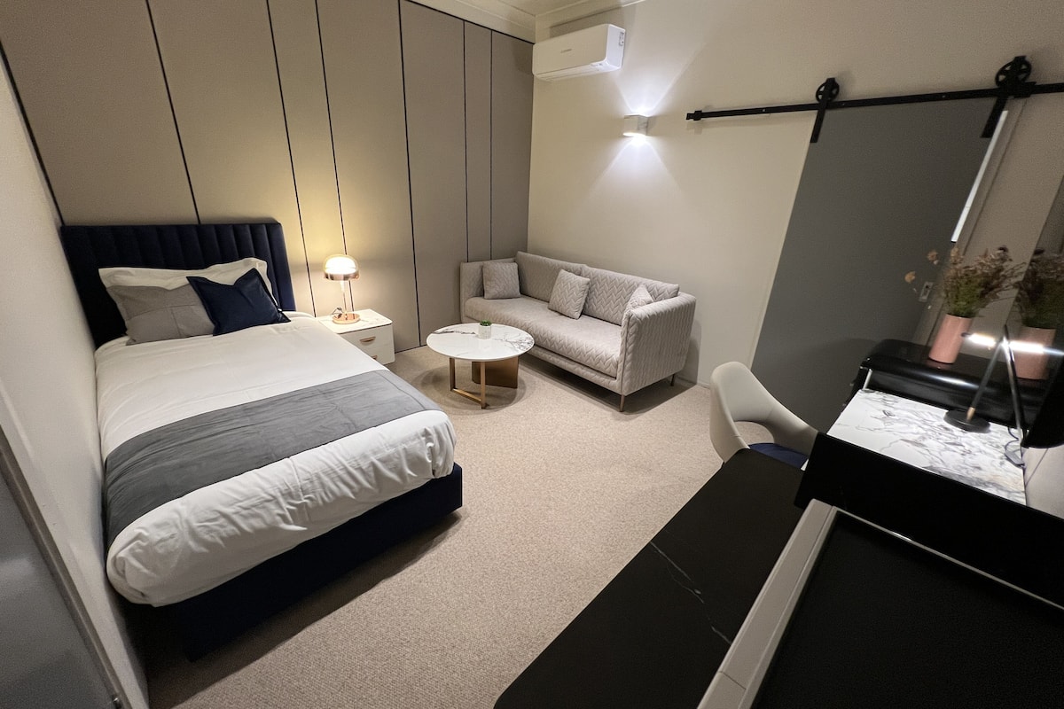 Une chambre d’hôtel moderne avec un grand lit, un canapé, une petite table ronde et un bureau avec une chaise.