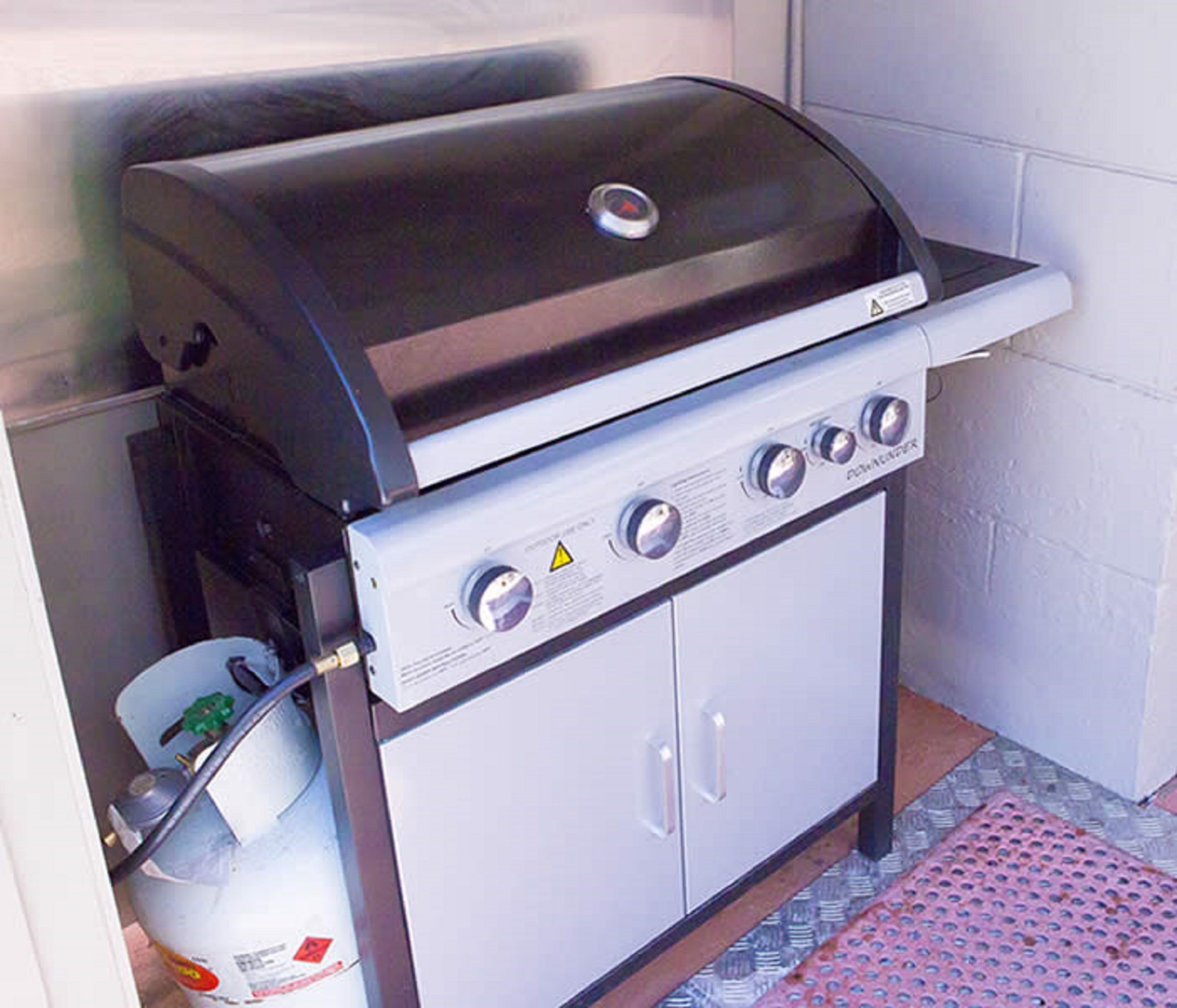 Una griglia a gas portatile con quattro fuochi, un pannello di controllo e un pensile.