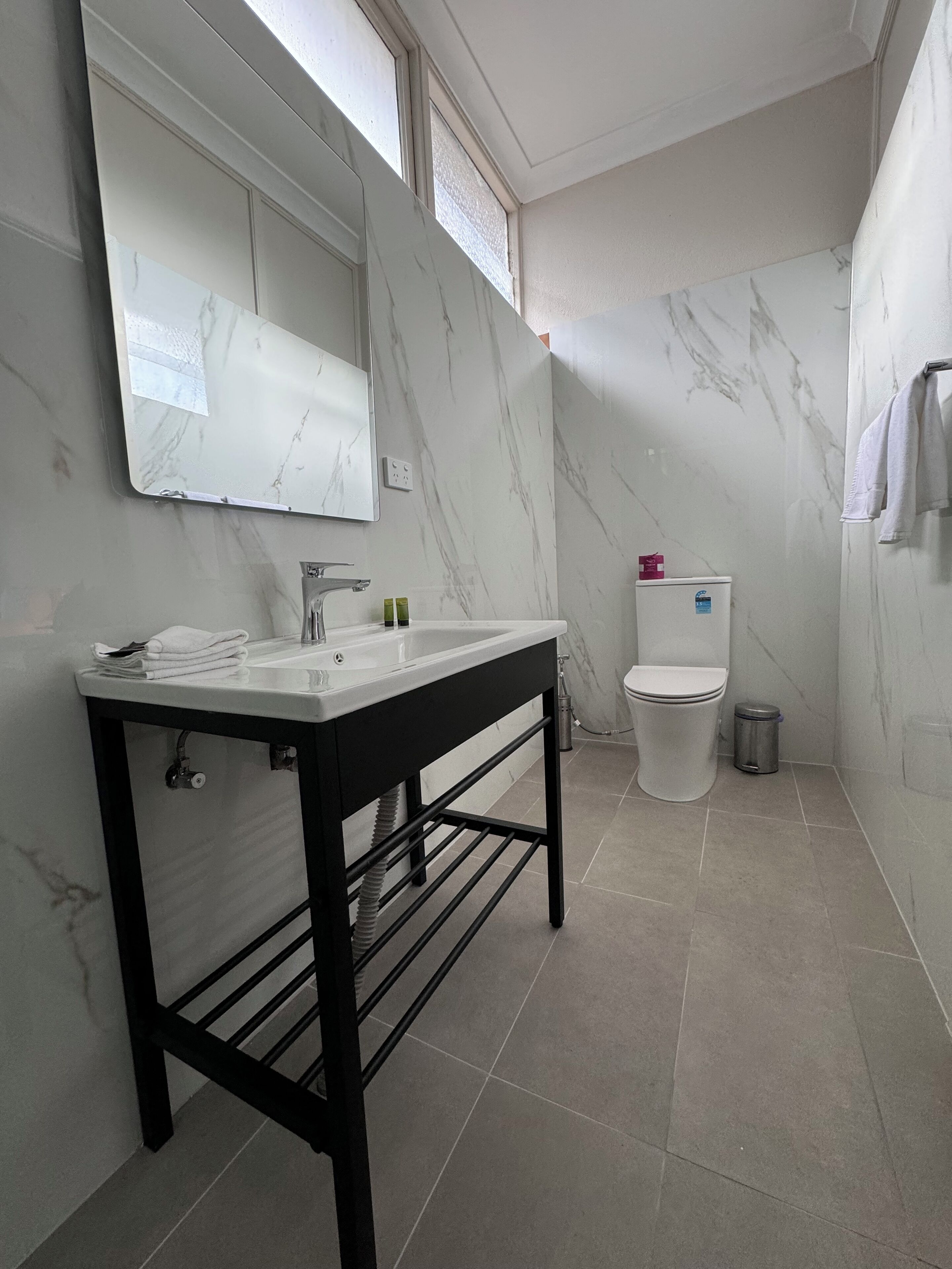 Un baño con lavamanos, espejo e inodoro blancos.