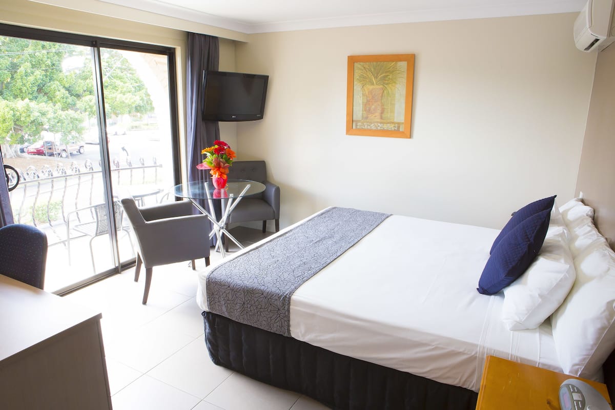 Une chambre d’hôtel équipée d’un lit, d’un bureau, d’une chaise, d’une télévision et d’une fenêtre donnant sur l’extérieur.