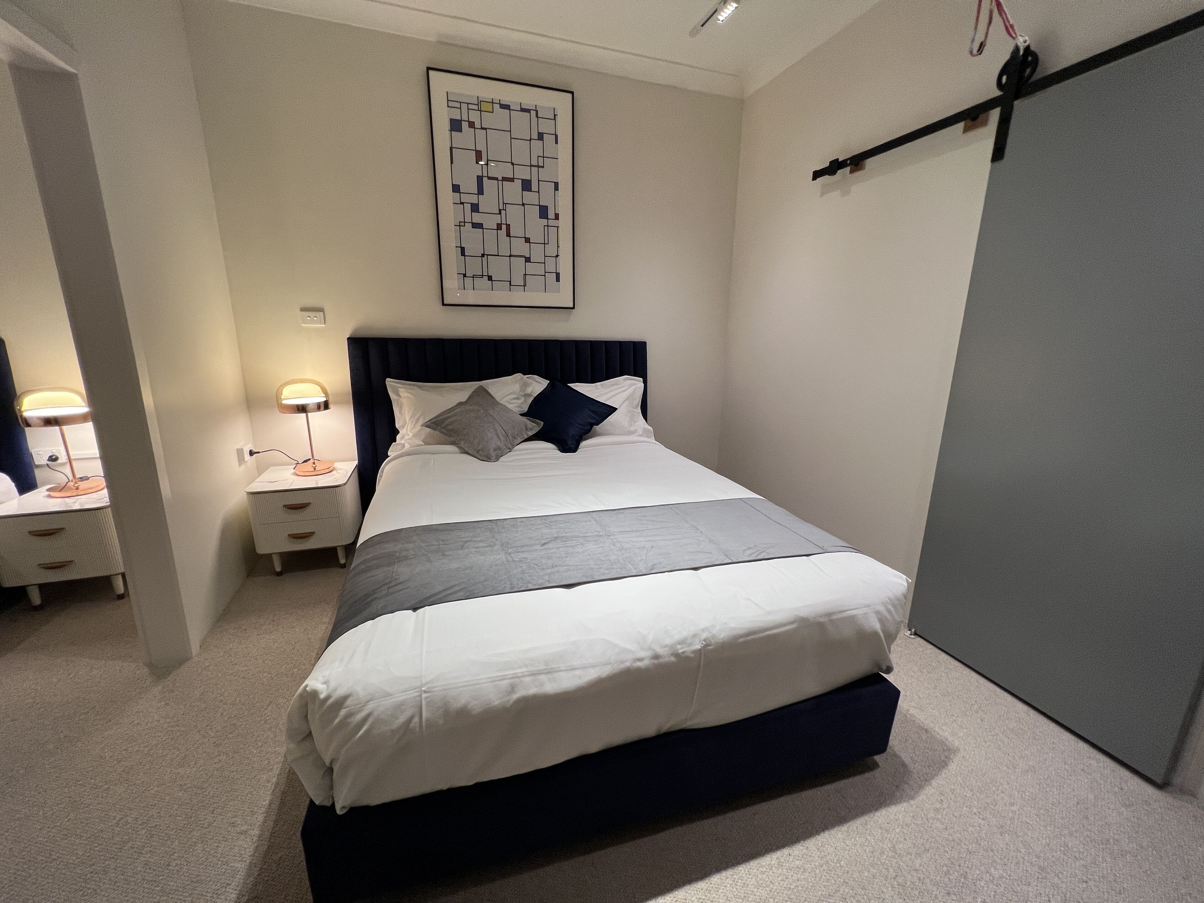 Un dormitorio ordenado con cama, mesitas de noche y una obra de arte colgada en la pared.