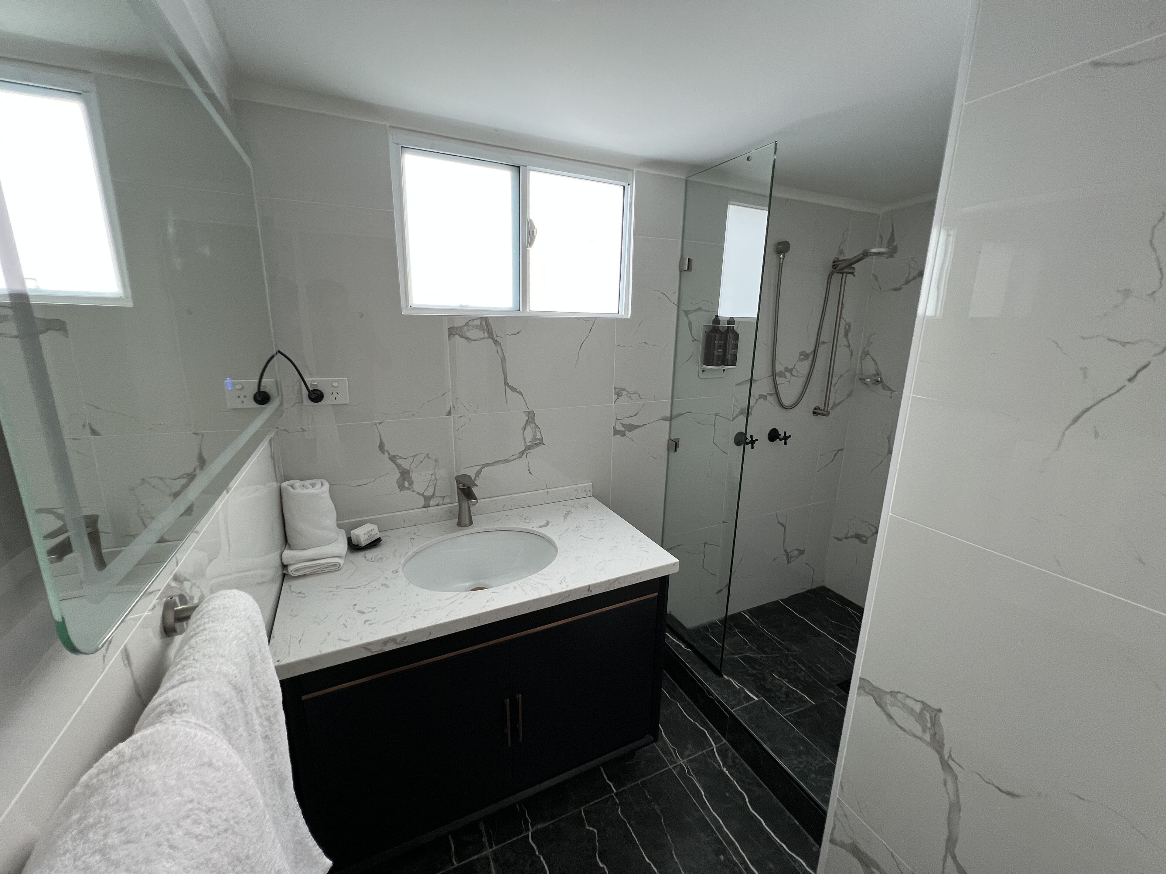Un baño moderno con tocador de mármol, cabina de ducha de vidrio y un espejo grande.