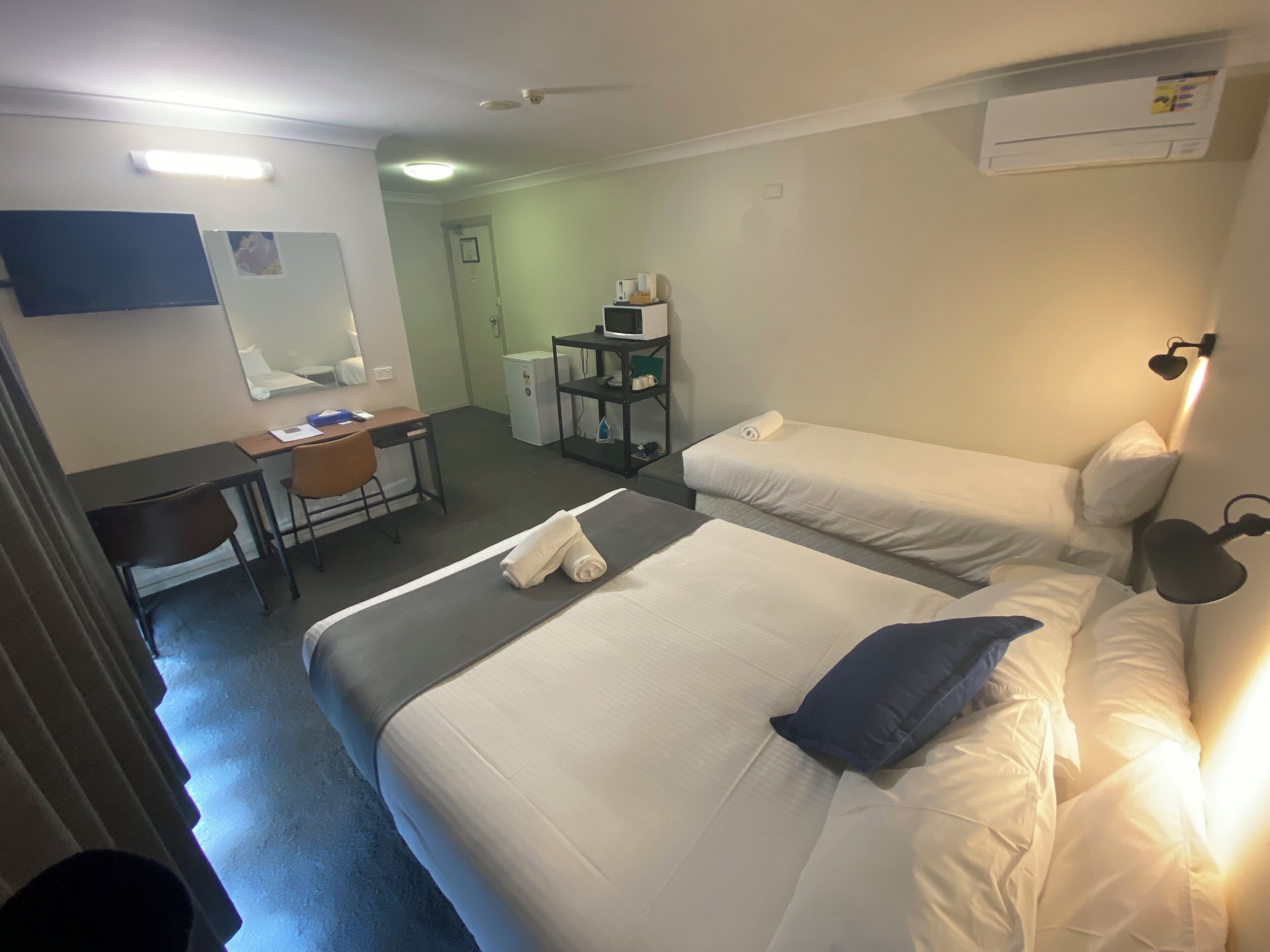 Hotelkamer met twee bedden, een bureau, een stoel, een klein tafeltje, een spiegel en een wandairconditioner.
