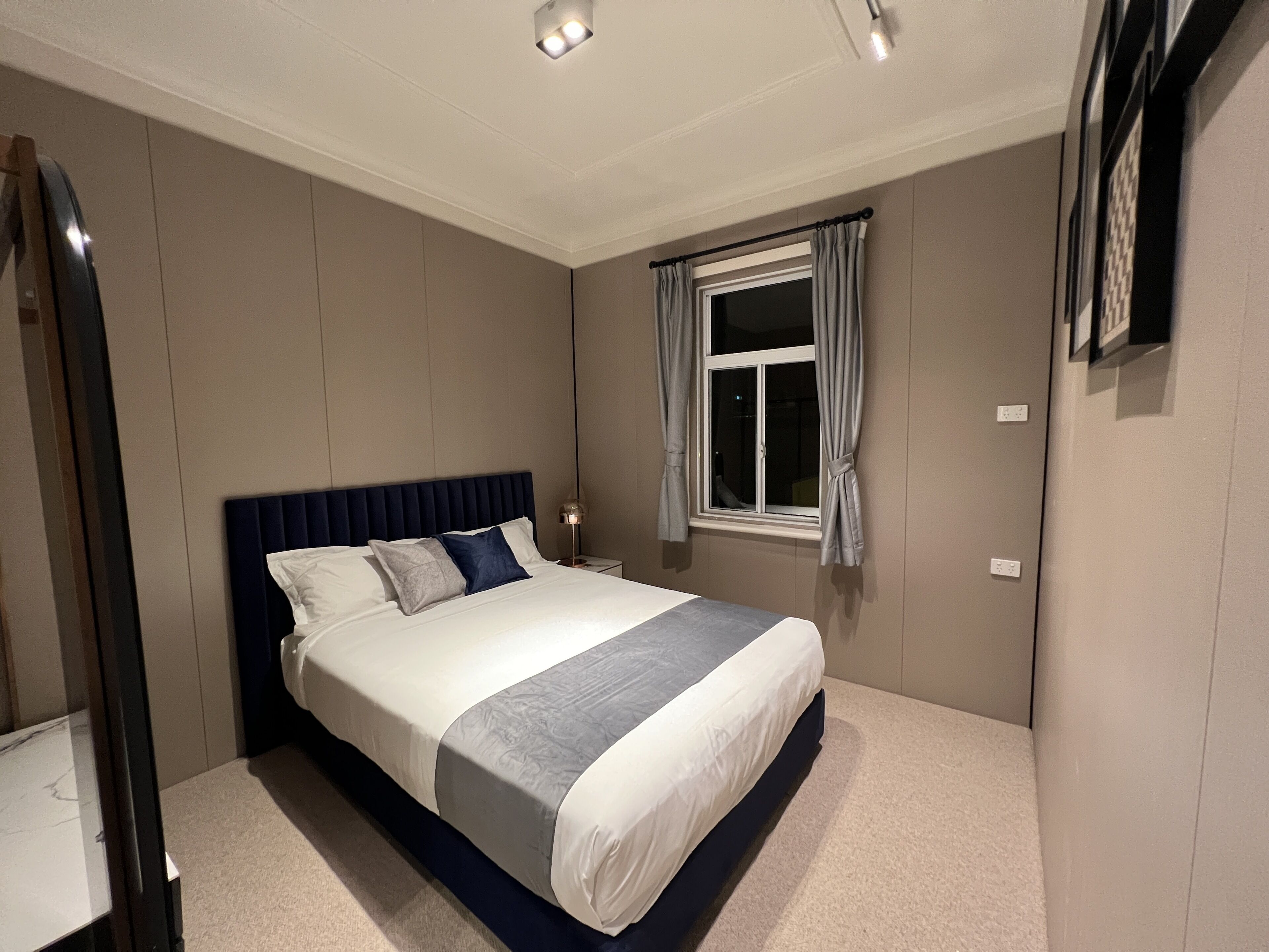 A bedroom with a bed, a nightstand, a window with curtains, and a mirror on the wall.