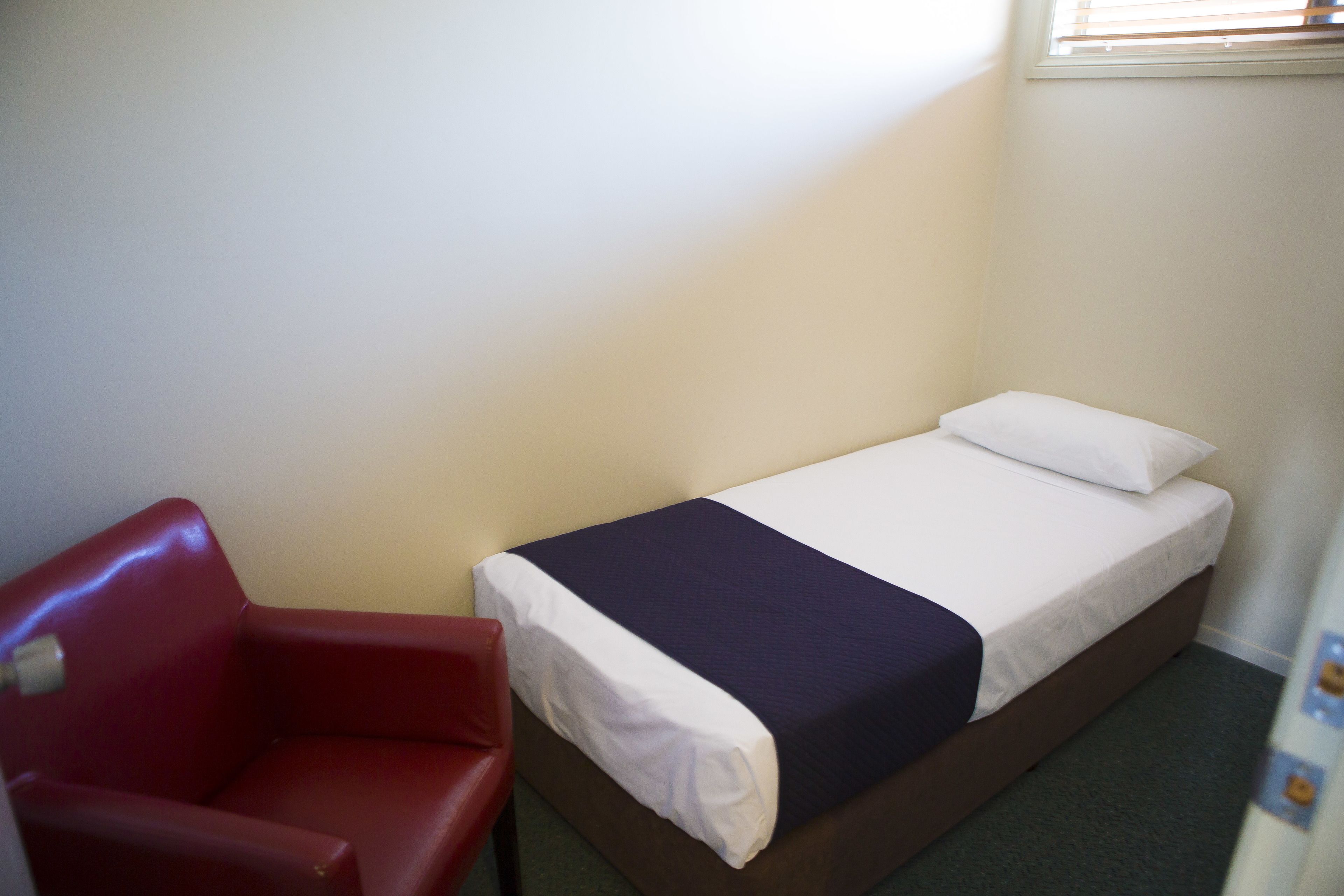 A small, single-bed room with a red chair and a white bedspread.