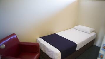 A small, single-bed room with a red chair and a white bedspread.