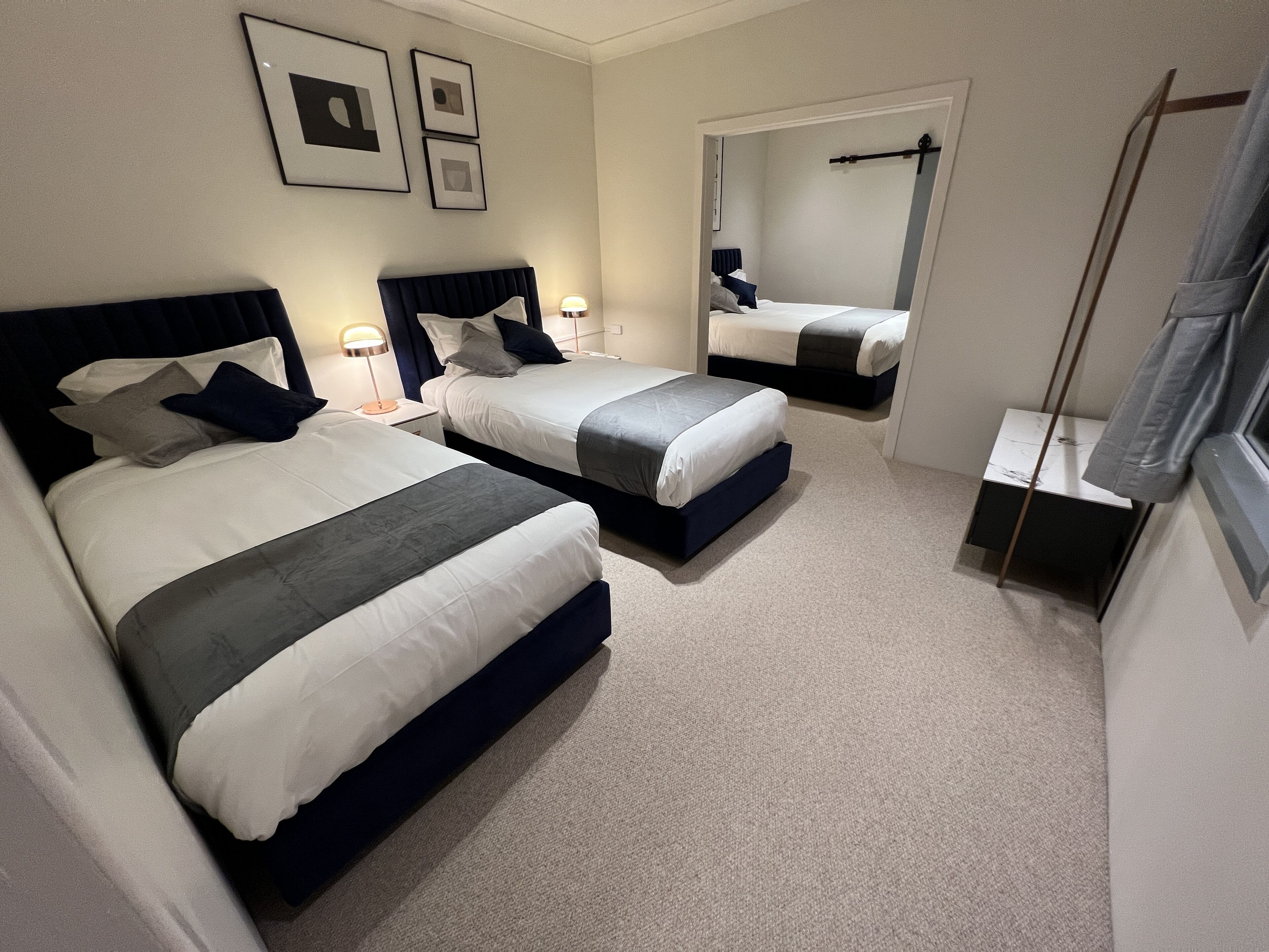 A hotel room with two beds, a small table, a mirror, and a window with a curtain.