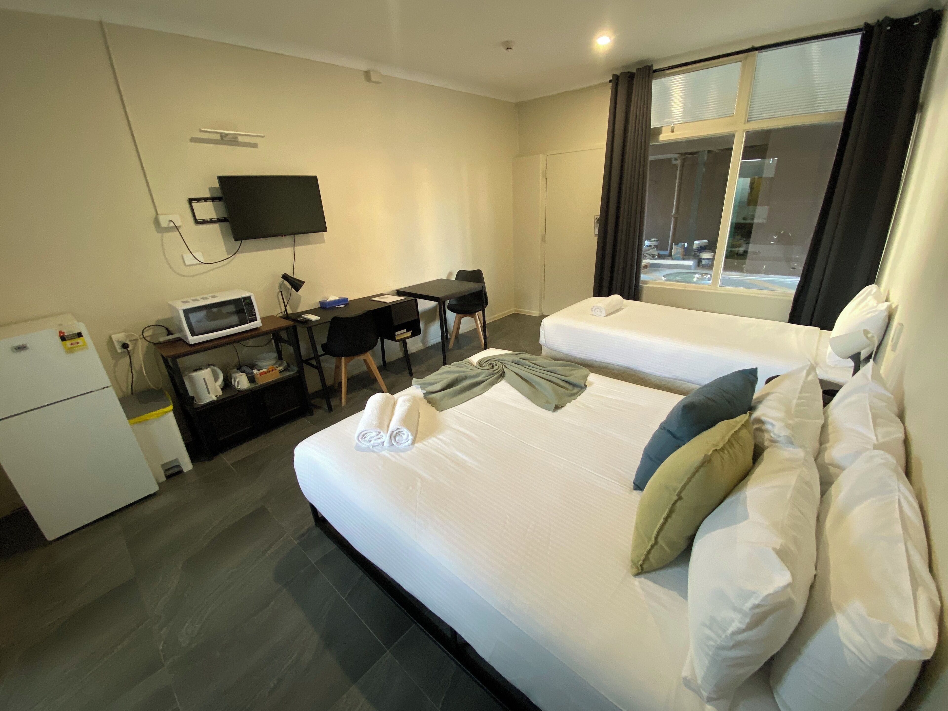 Habitación de hotel con dos camas, un escritorio, un televisor de pantalla plana, un microondas y un refrigerador.