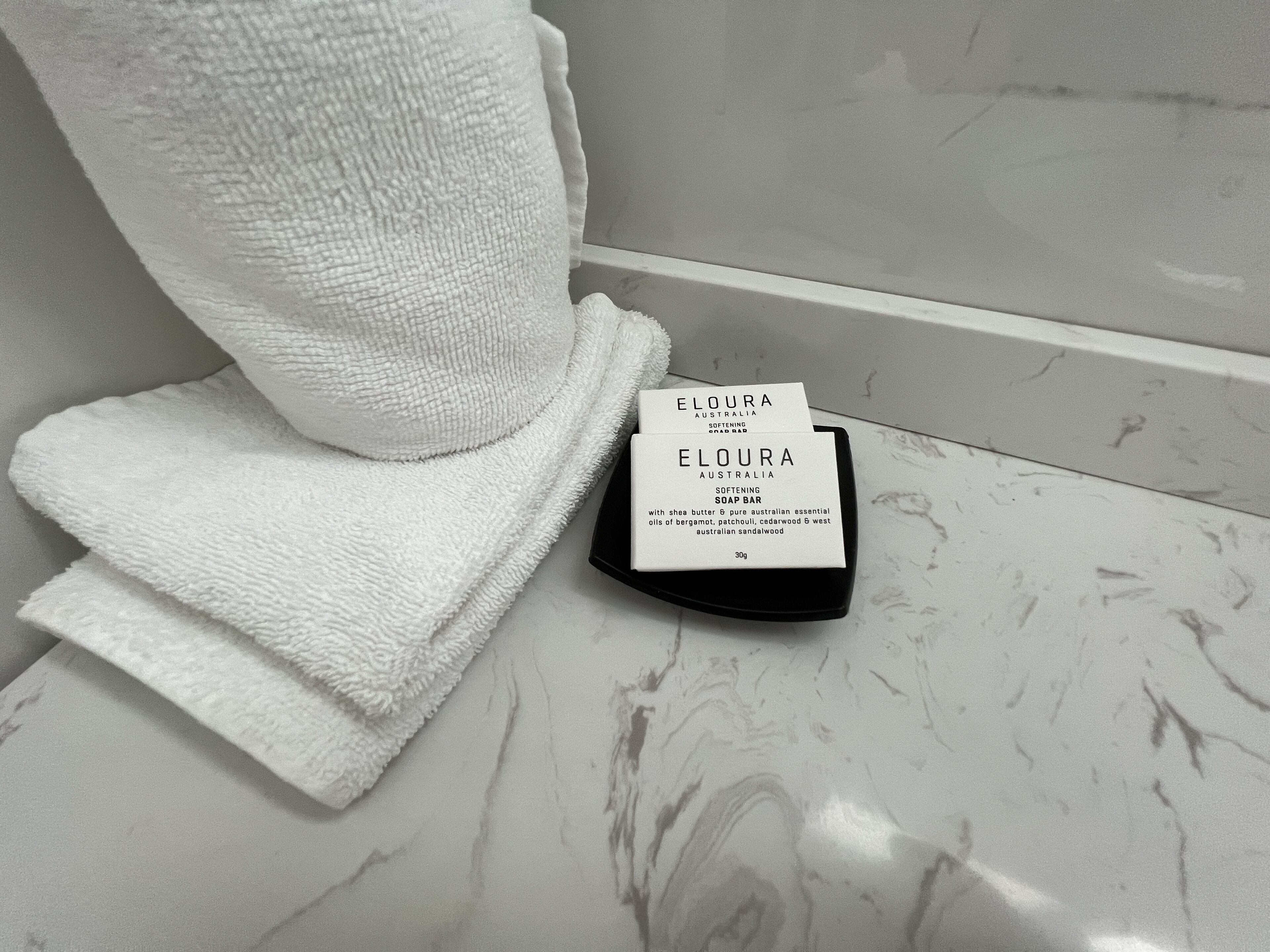 Un baño con una toalla blanca y una barra de jabón ELOURA Australia sobre una encimera de mármol.