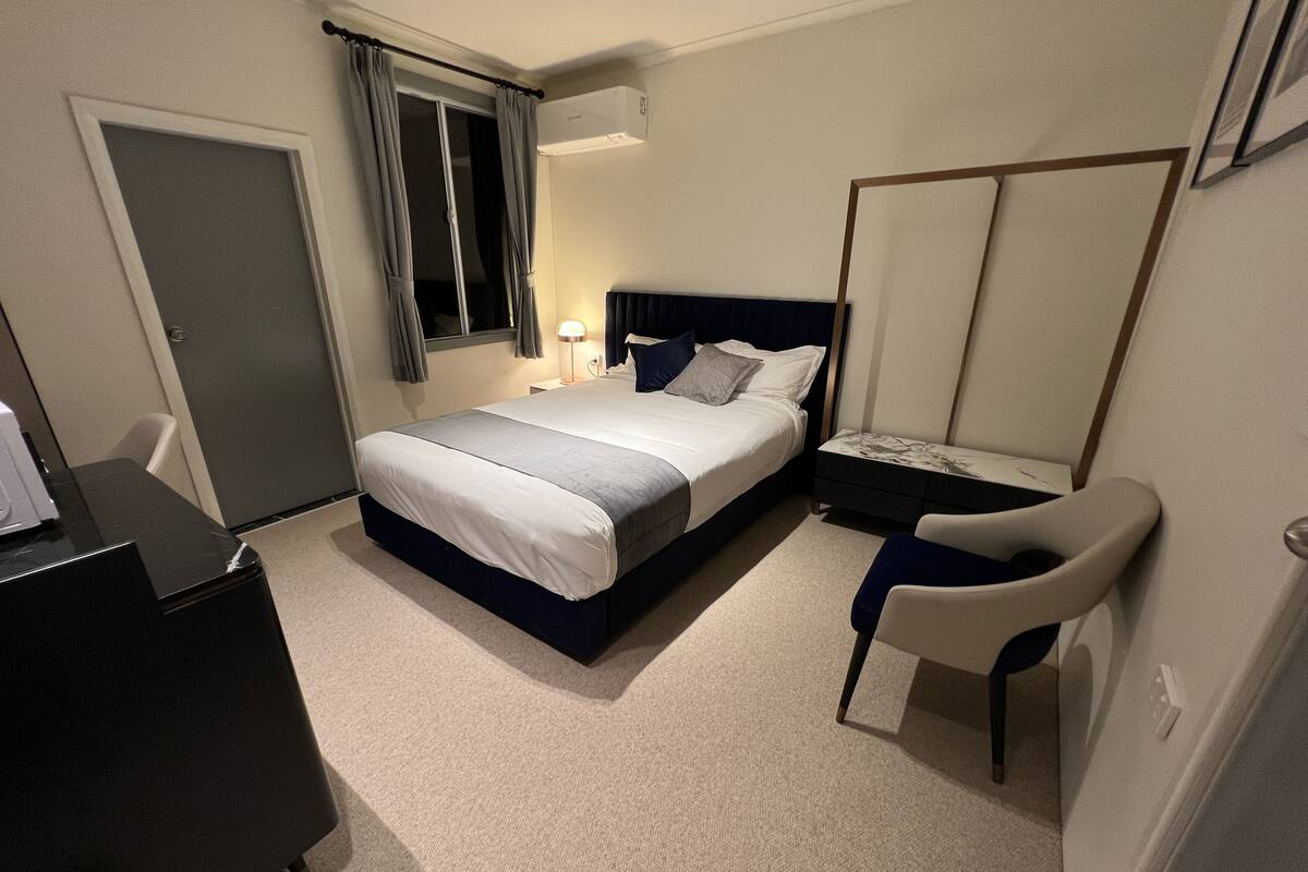 Une chambre d’hôtel comprenant un lit, un bureau, une chaise, une armoire et une fenêtre avec des rideaux.