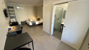 A modern hotel room with a bed, a desk, and a chair. There is a bathroom visible through a glass door. - Lismore City Motor Inn (Lismore)